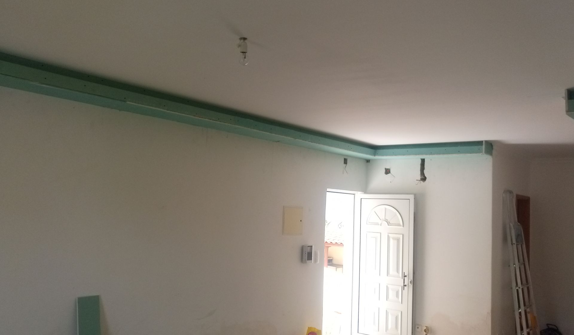 Quarto interior com detalhes verdes nas bordas do teto, paredes brancas e uma porta ao fundo.
