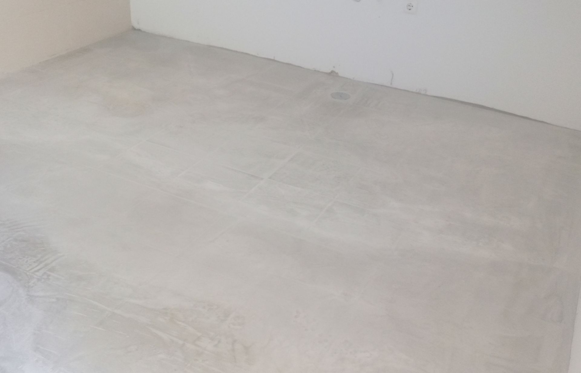 Piso de concreto cinza claro e sem acabamento em uma sala vazia, ao lado de paredes brancas.