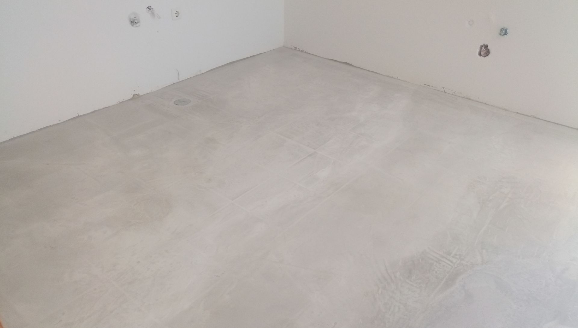 Sala vazia com piso de concreto cinza claro e paredes brancas.