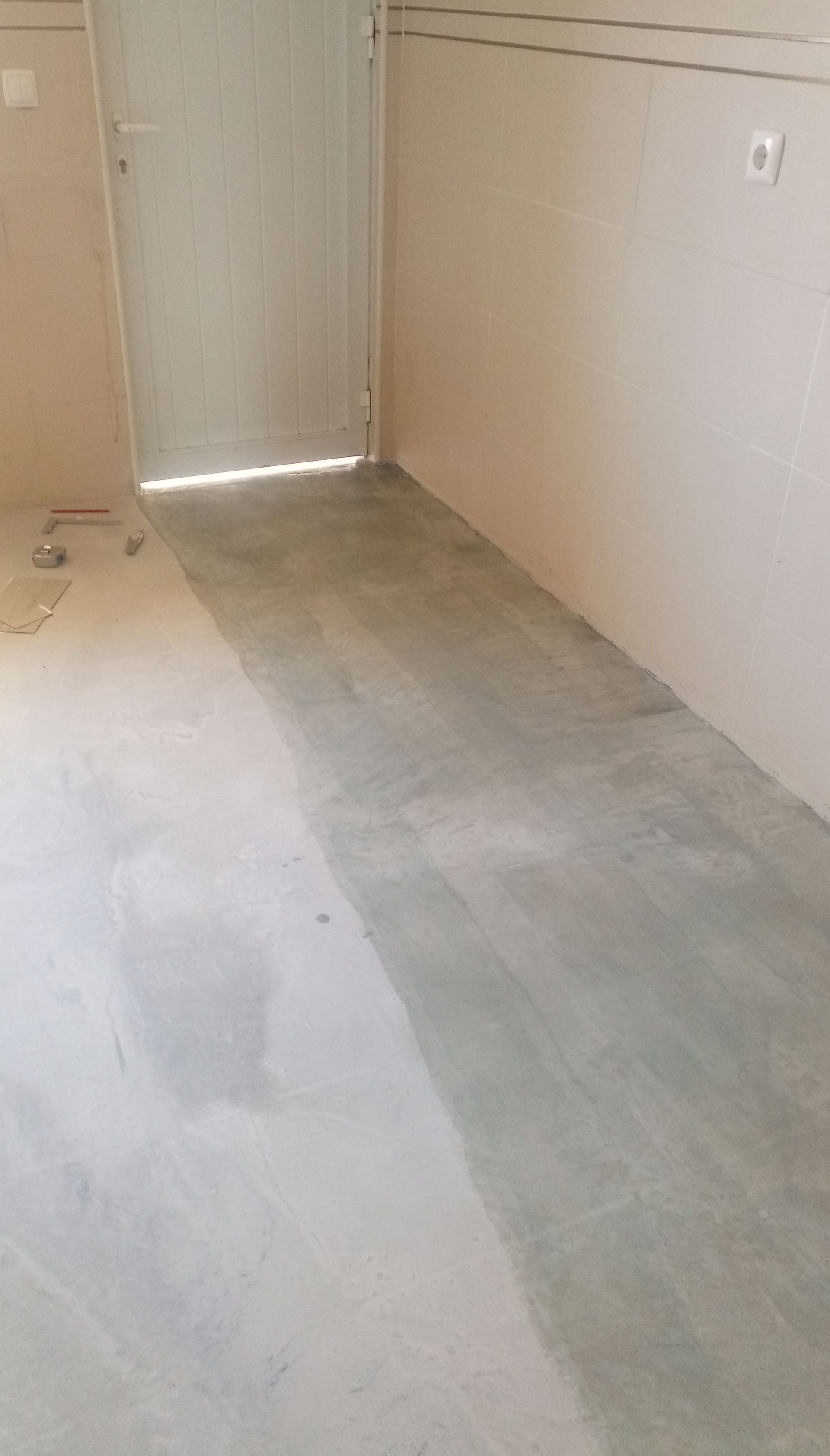 Um quarto com piso de concreto, porta fechada e paredes de cor clara.