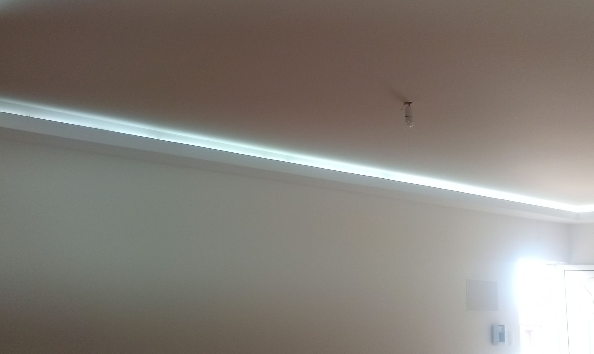 Um quarto com teto branco, moldura decorativa e iluminação LED brilhante, e uma parede branca banhada de luz solar.