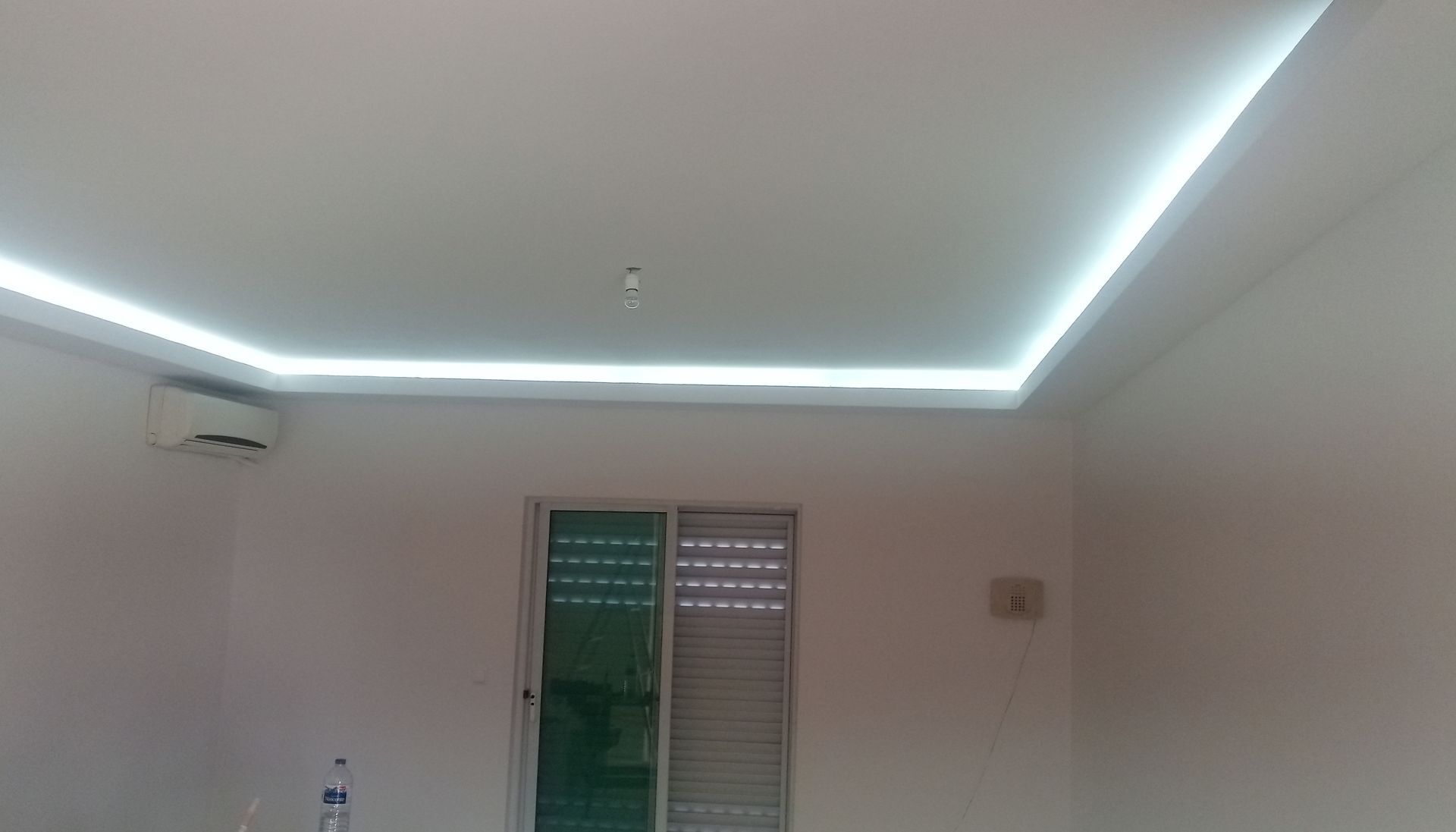 Quarto com teto branco, iluminação LED embutida, janela e ar condicionado.