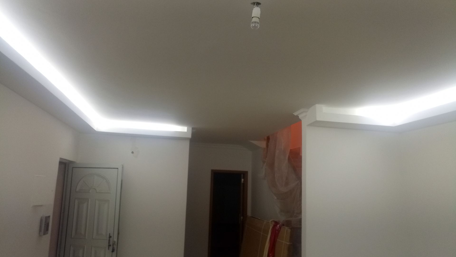 Quarto branco com luzes embutidas no teto; porta à esquerda, corredor nos fundos.