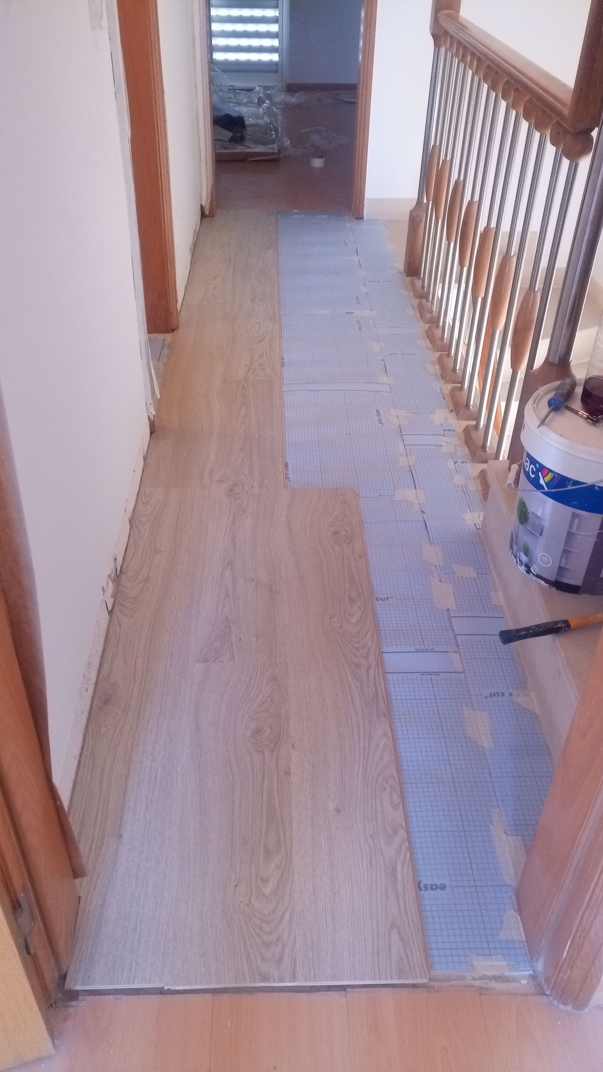 Corredor com piso parcialmente instalado imitando madeira clara. A escada com corrimão de madeira fica à direita.