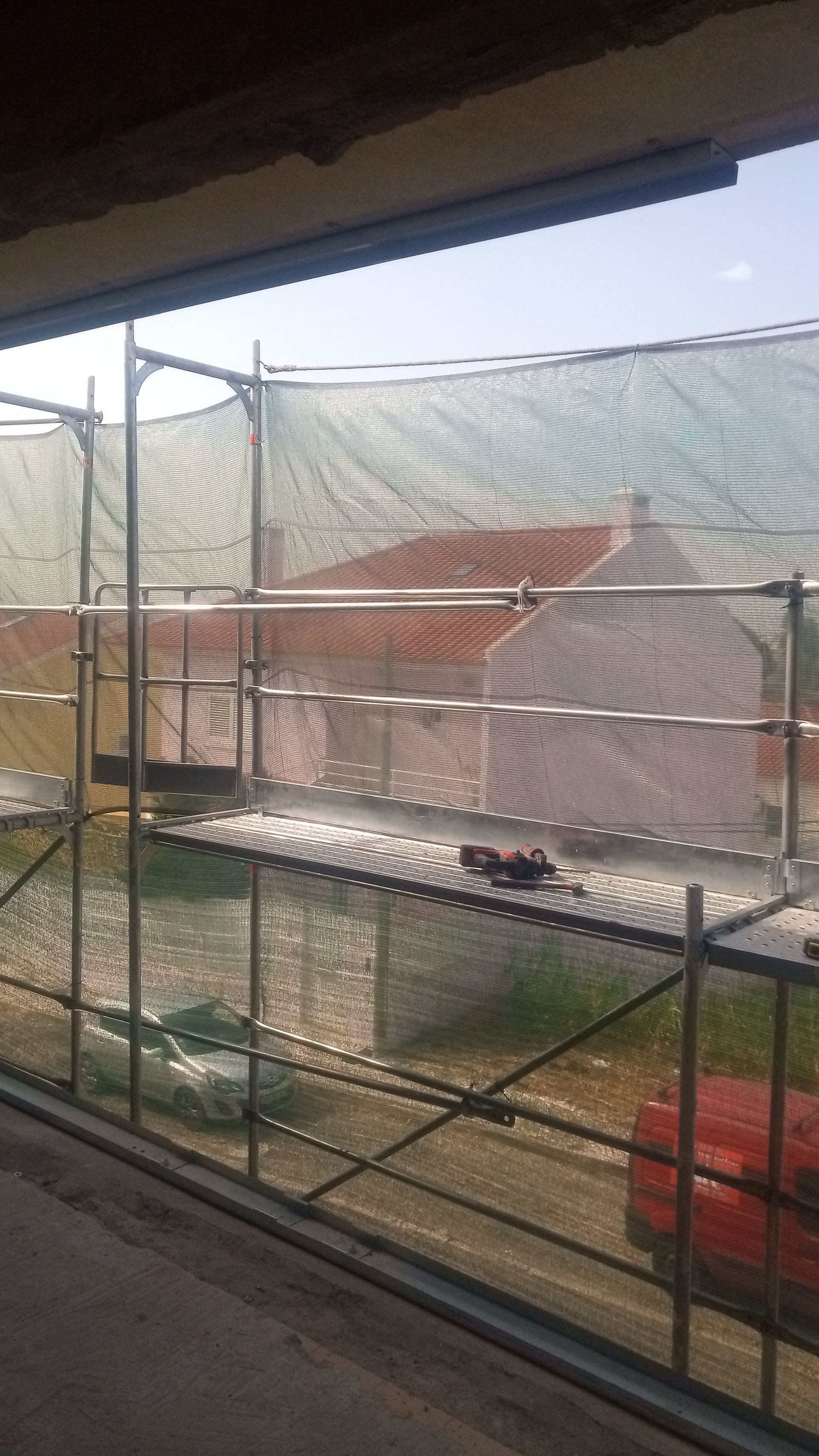 Andaimes com redes de segurança em frente a um edifício, obscurecendo parcialmente a vista das casas e do céu.