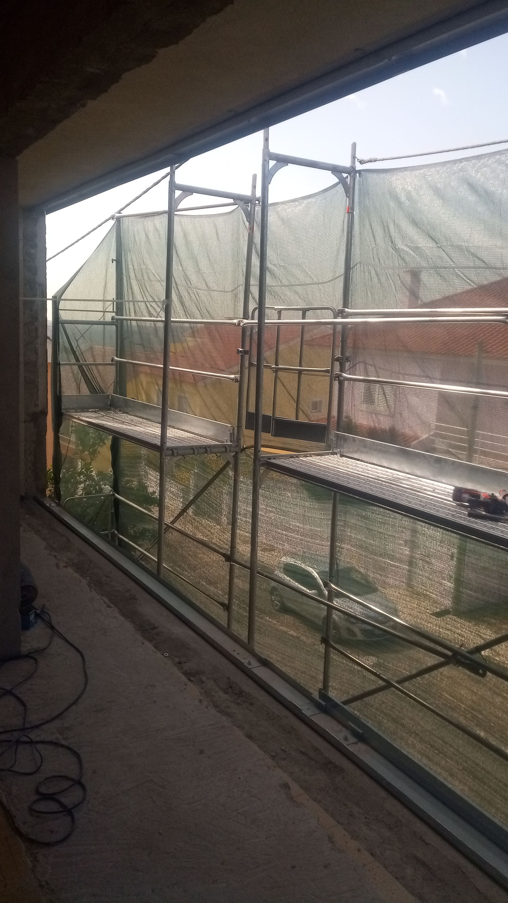 Andaimes com redes de proteção dentro da abertura de uma janela, possivelmente para construção ou reforma.