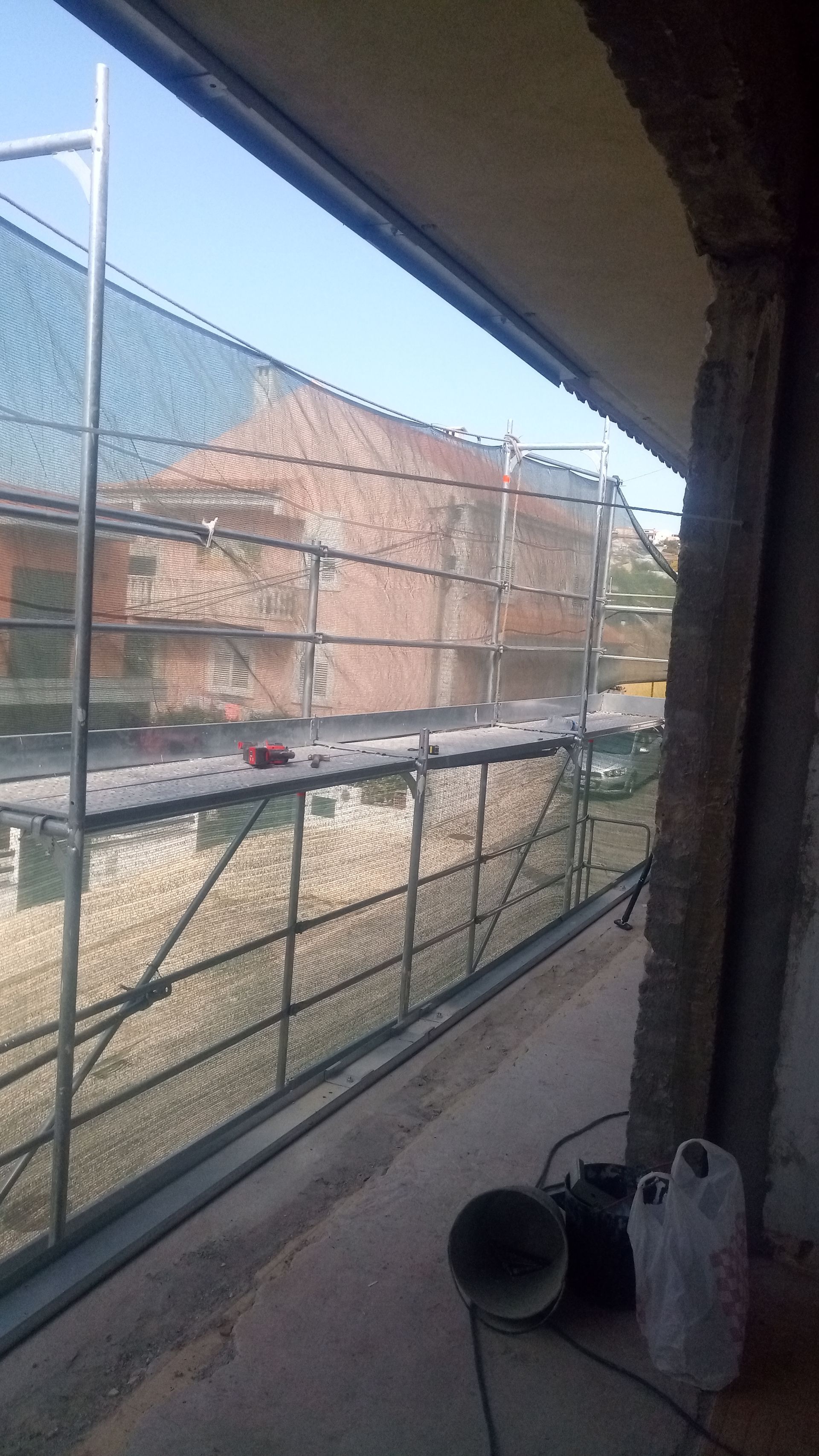 Andaimes com redes de segurança em frente a um prédio, vistos de uma varanda.