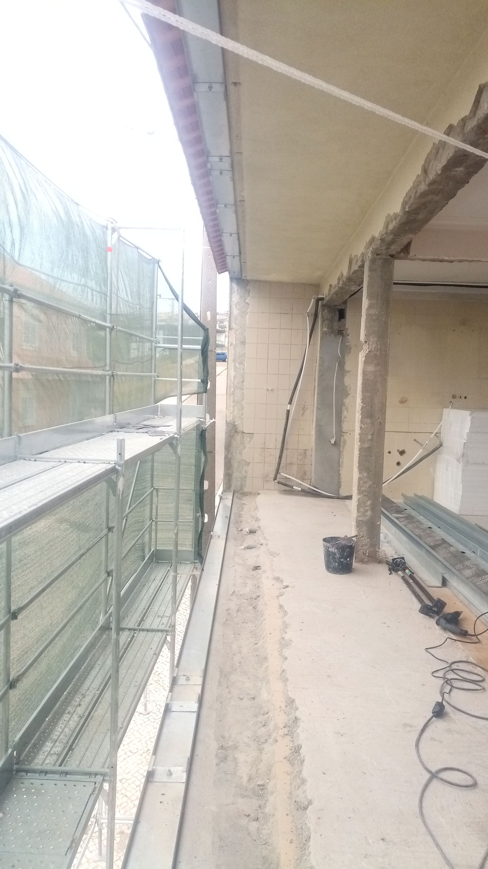 Andaimes montados ao longo da fachada de um edifício em construção, com concreto aparente e uma cobertura saliente.