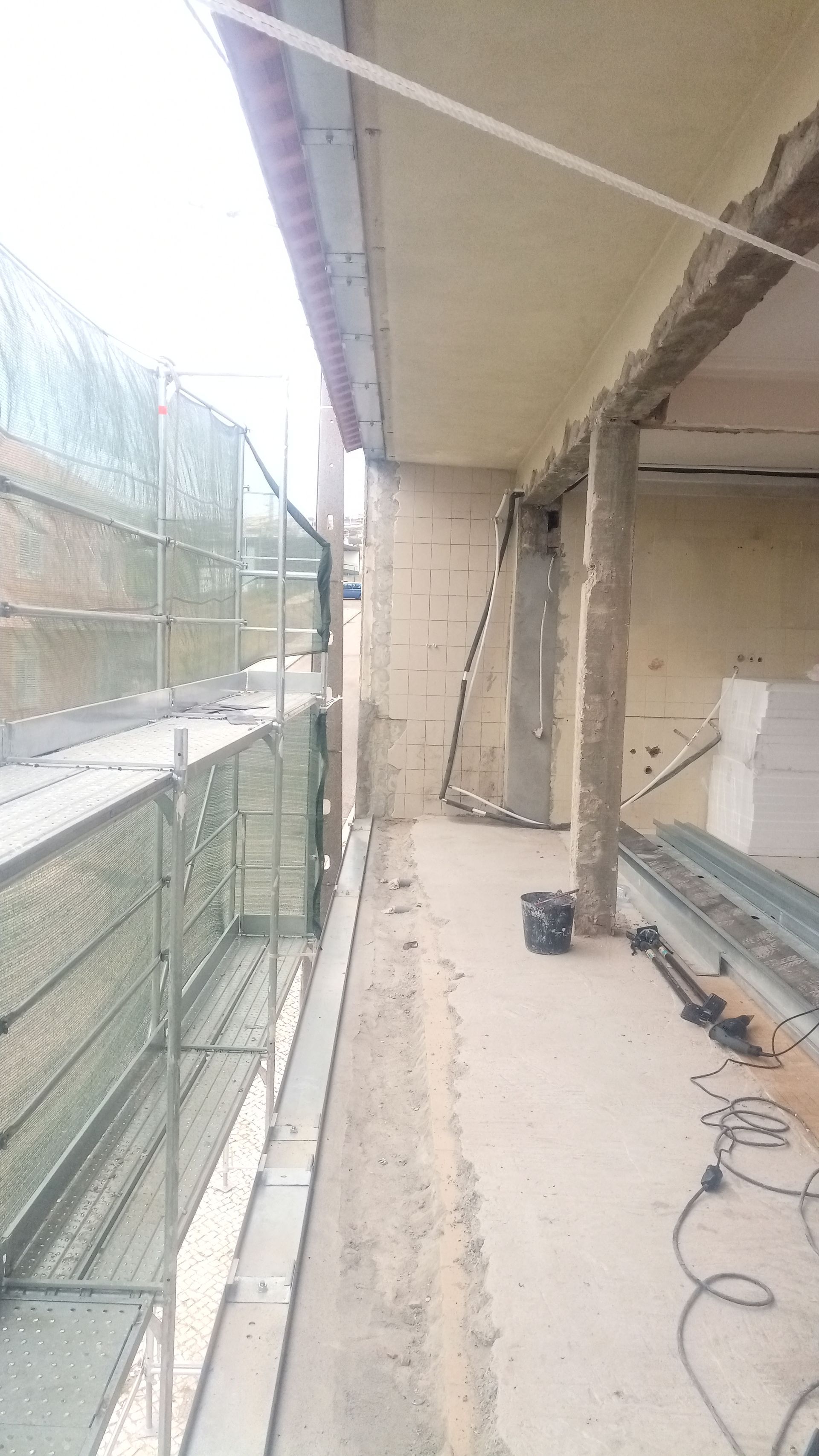 Canteiro de obras com andaimes. Trabalhos na fachada do edifício; concreto e isolamento aparentes.