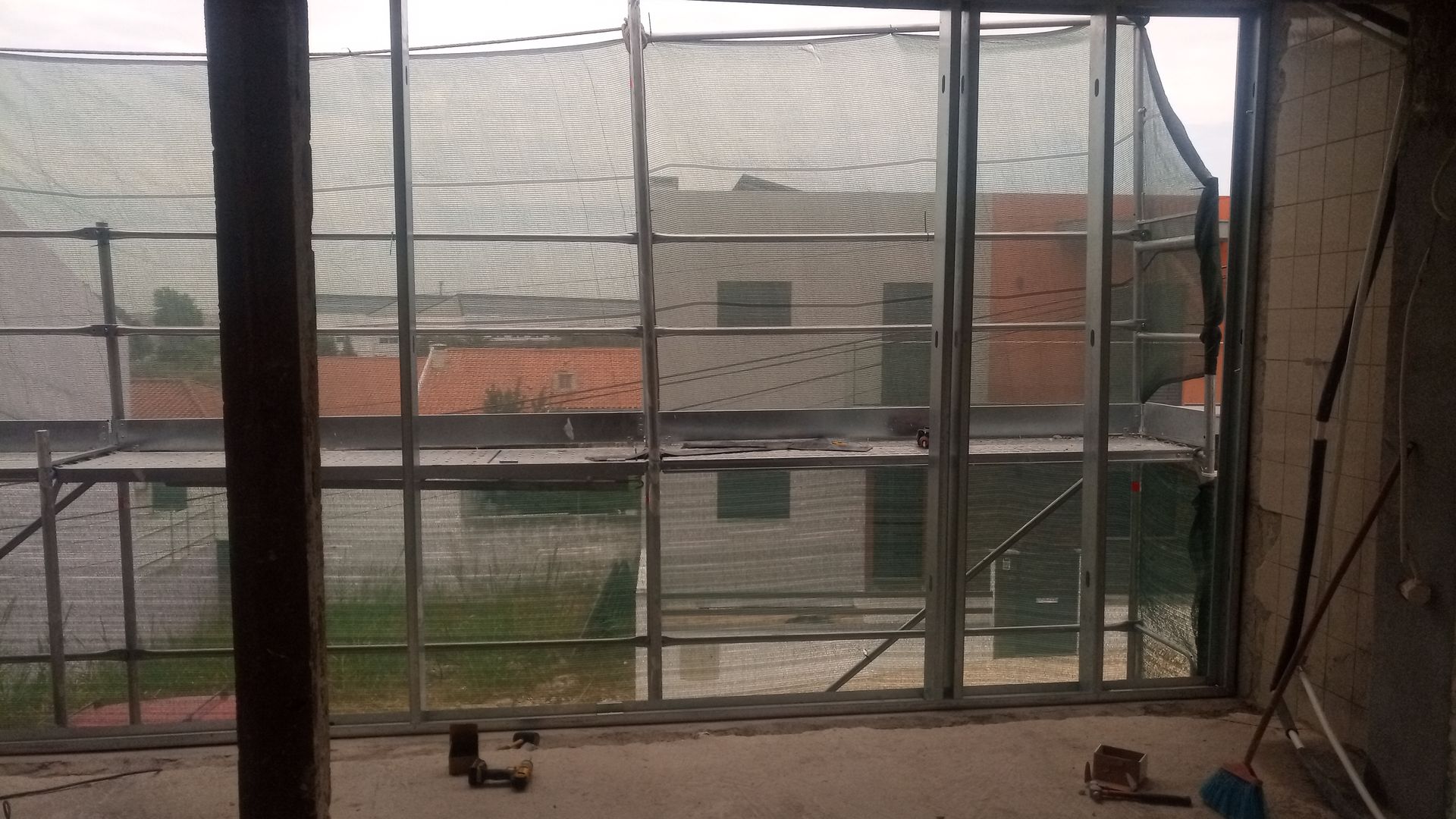 Vista interior de um edifício em construção, com uma grande janela mostrando um prédio do outro lado da rua.