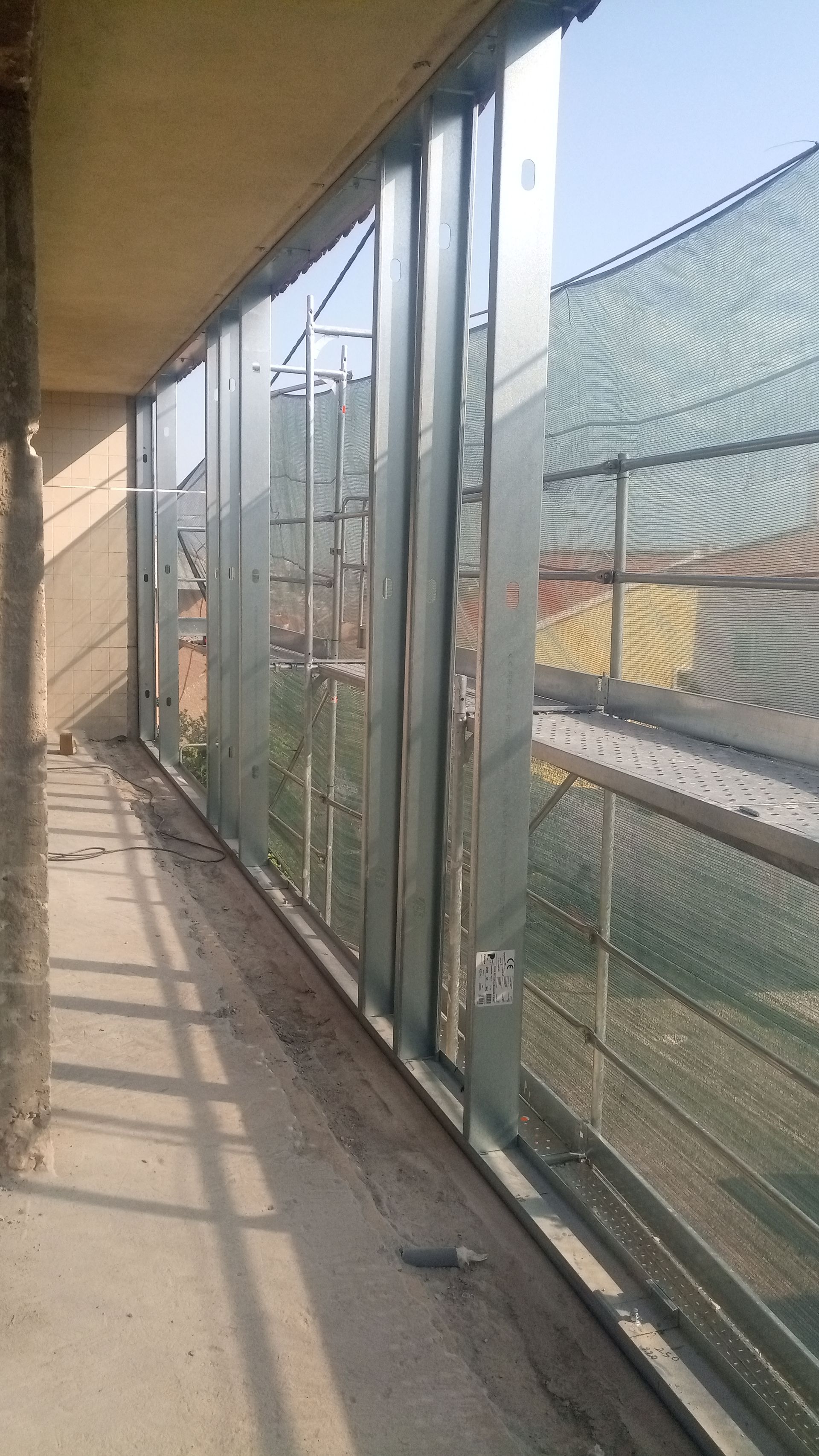 Varanda com estrutura metálica e tela de malha transparente, com vista para uma área externa ensolarada.