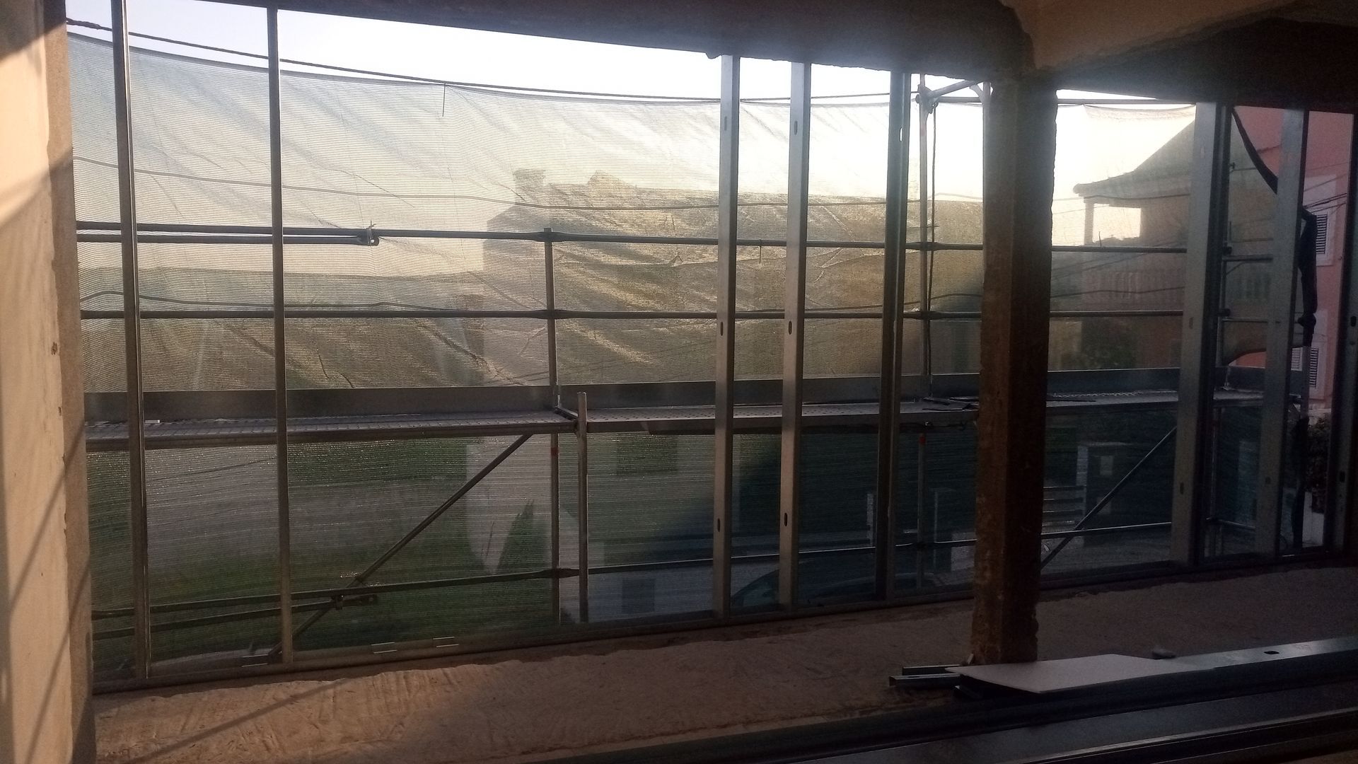 Janela com grade metálica, com vista para uma estrutura coberta por uma rede sob um céu nublado.