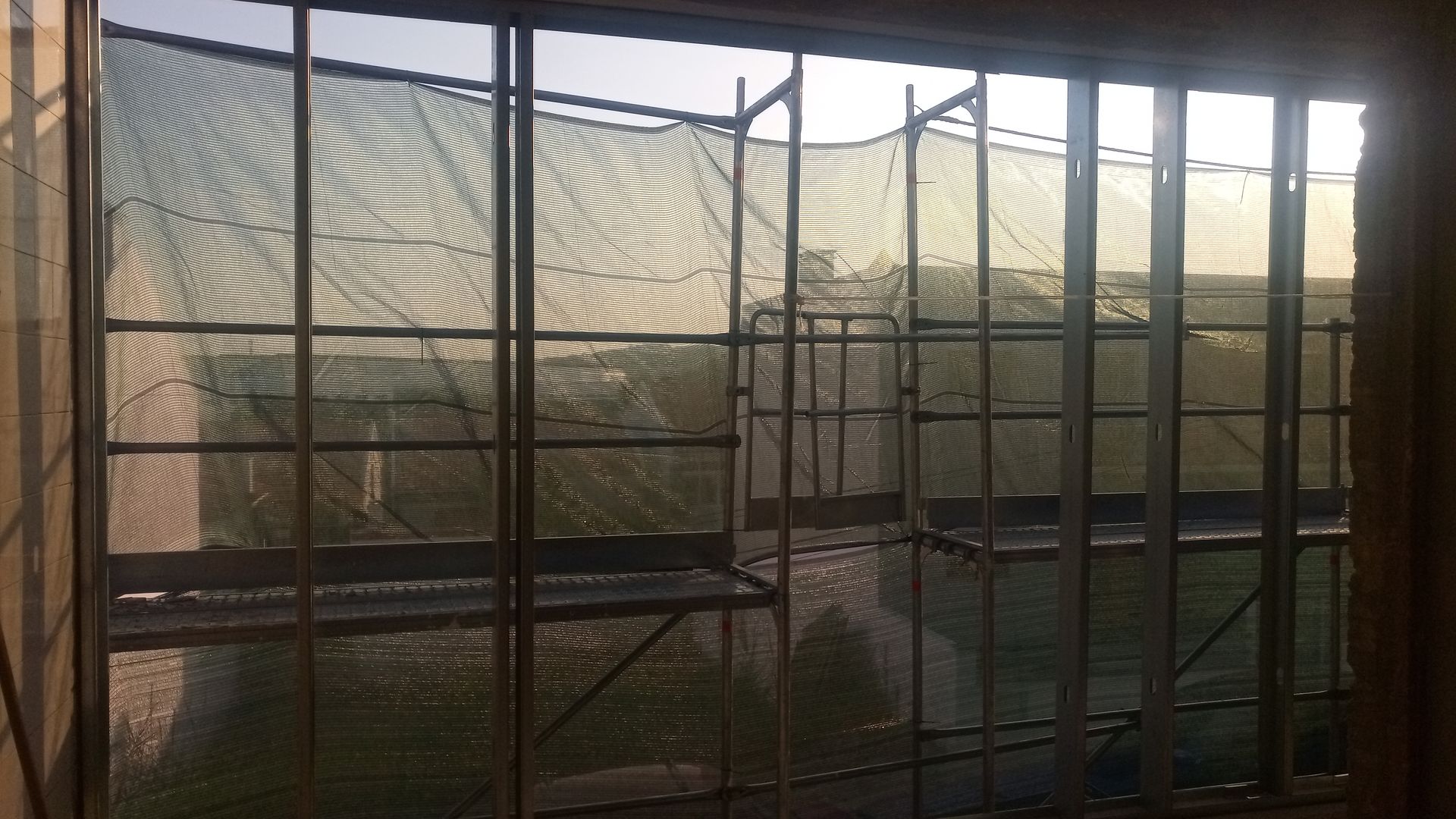 Janela com grades de metal e rede, com vista para uma paisagem externa enevoada.