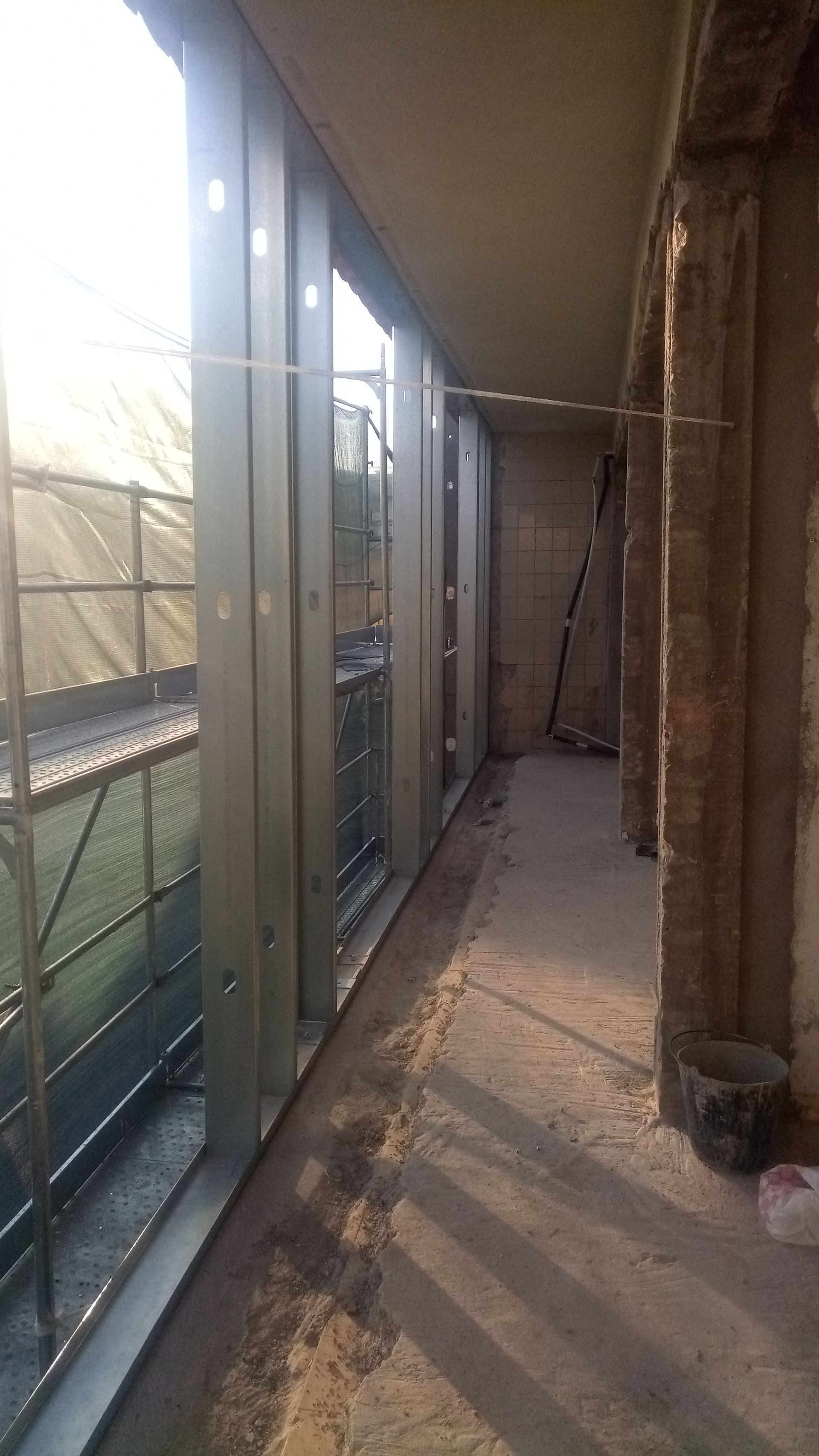 Vista interna de um canteiro de obras. Estrutura metálica para uma janela ou parede, com vista externa de uma tela de proteção.