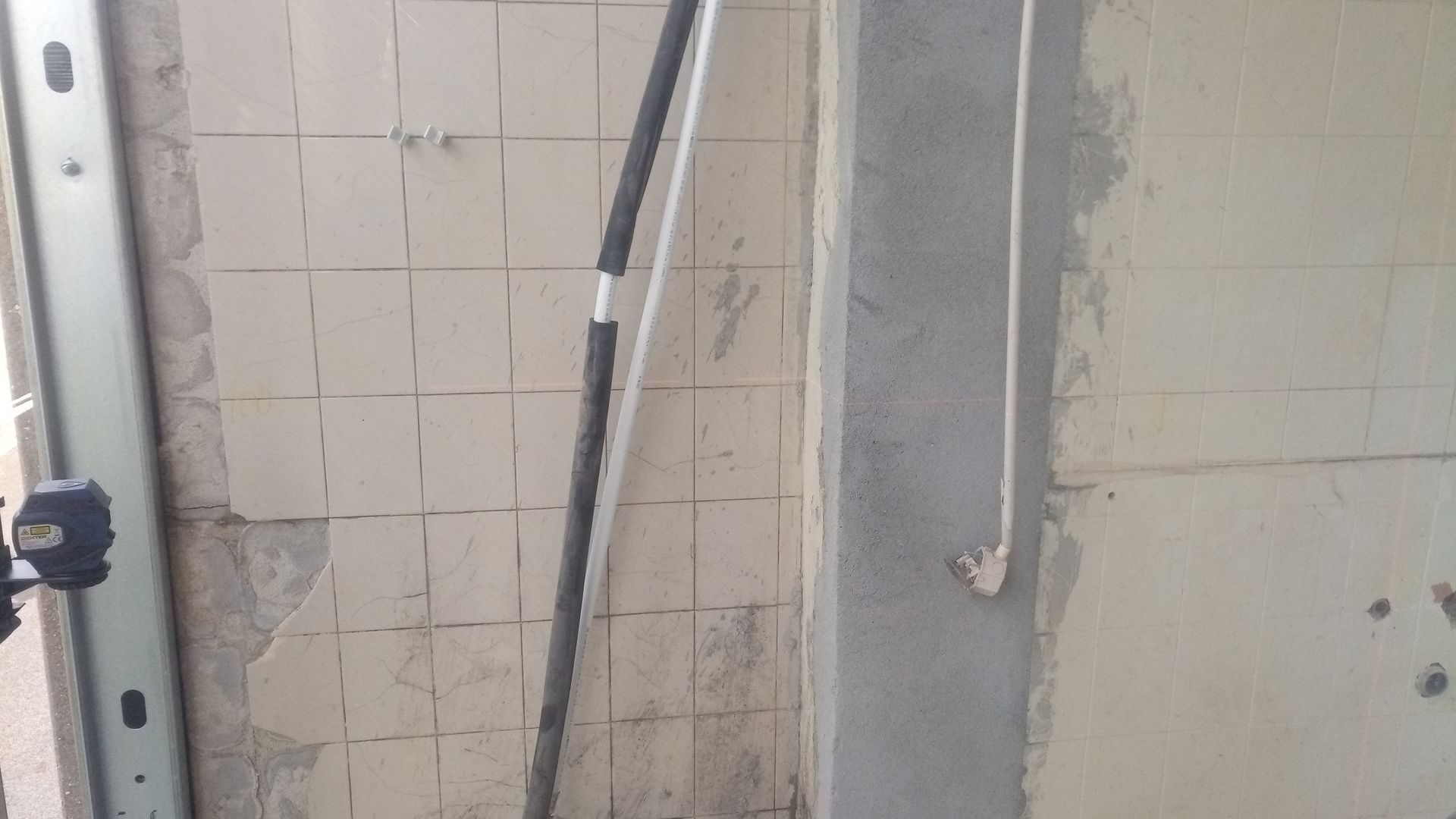 Vista interior de uma parede com azulejos expostos, um poste de metal e uma coluna vertical de concreto.