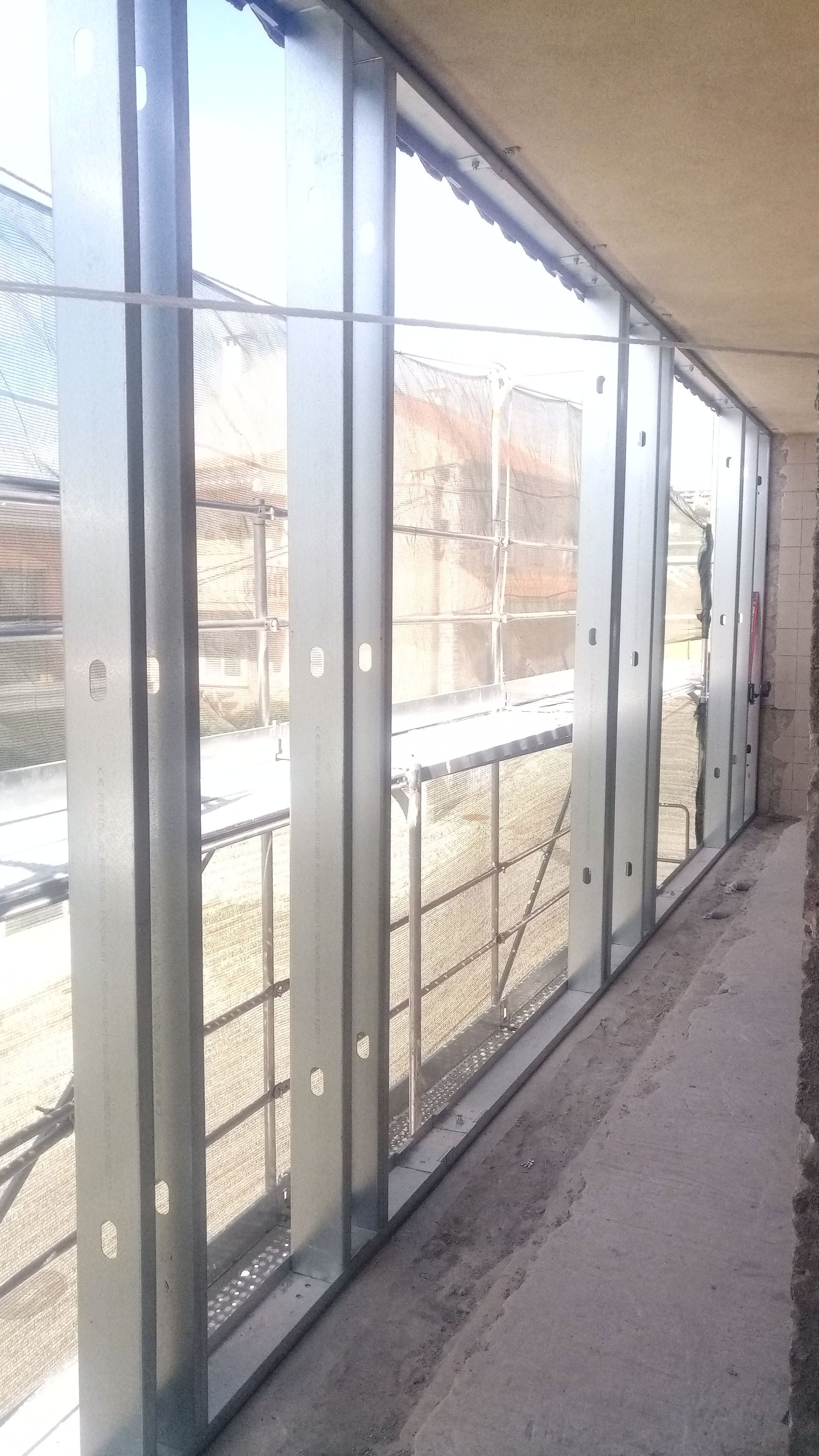 Canteiro de obras: Janelas com estrutura metálica parcialmente instaladas, mostrando uma vista do exterior com cerca.