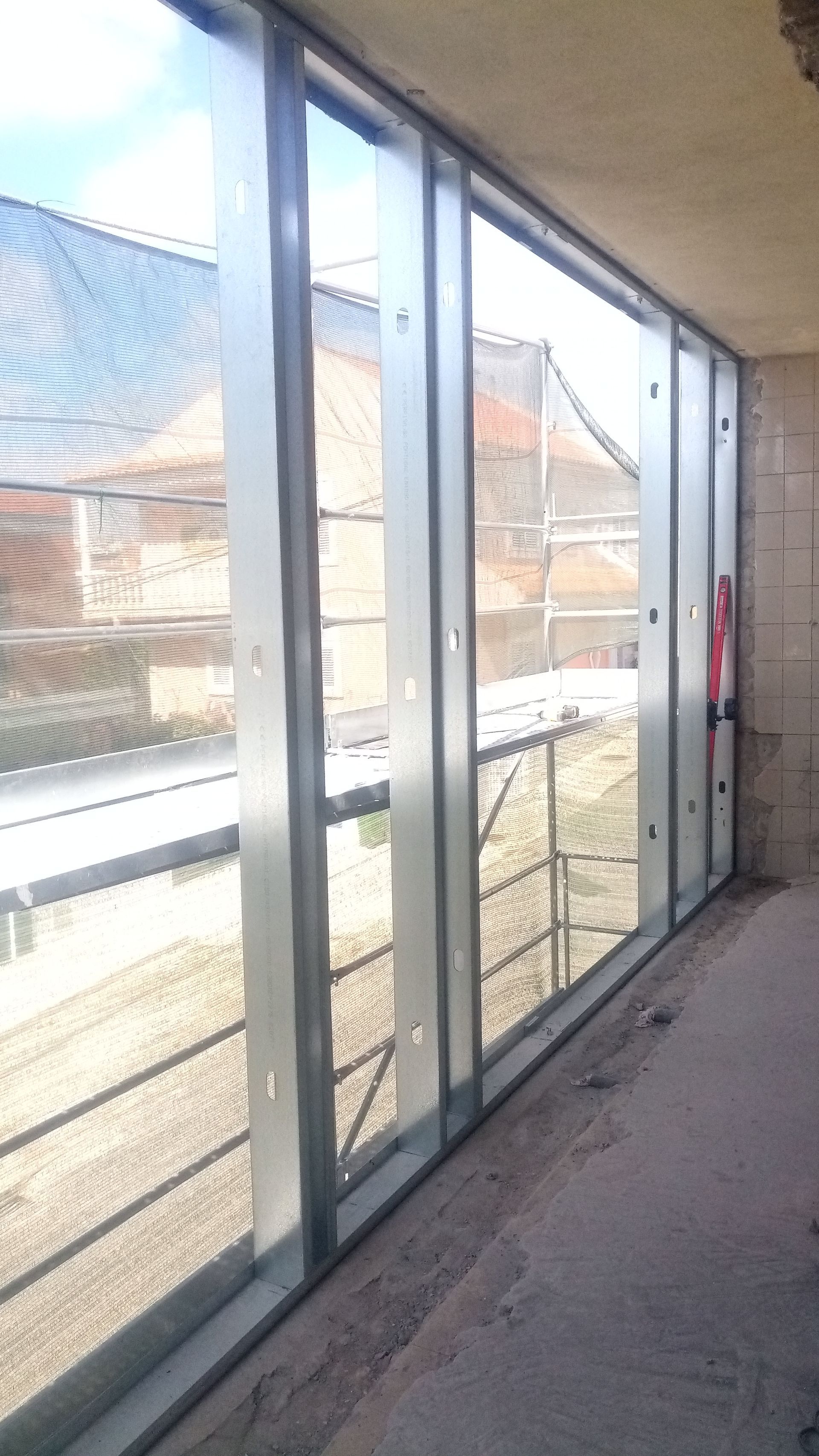 Vista exterior através de uma janela de vidro parcialmente instalada em um edifício em construção.