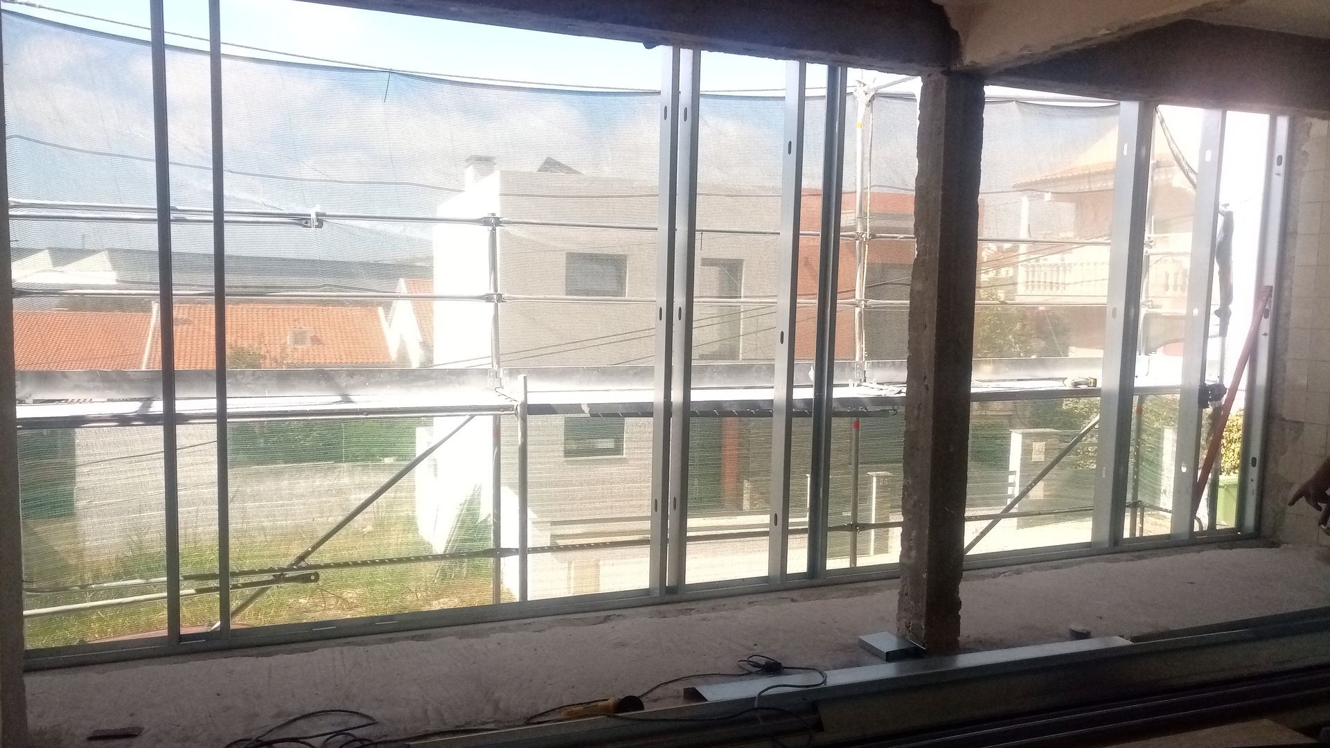 Vista interior de um edifício com grandes janelas, construção inacabada e vista para os edifícios exteriores.