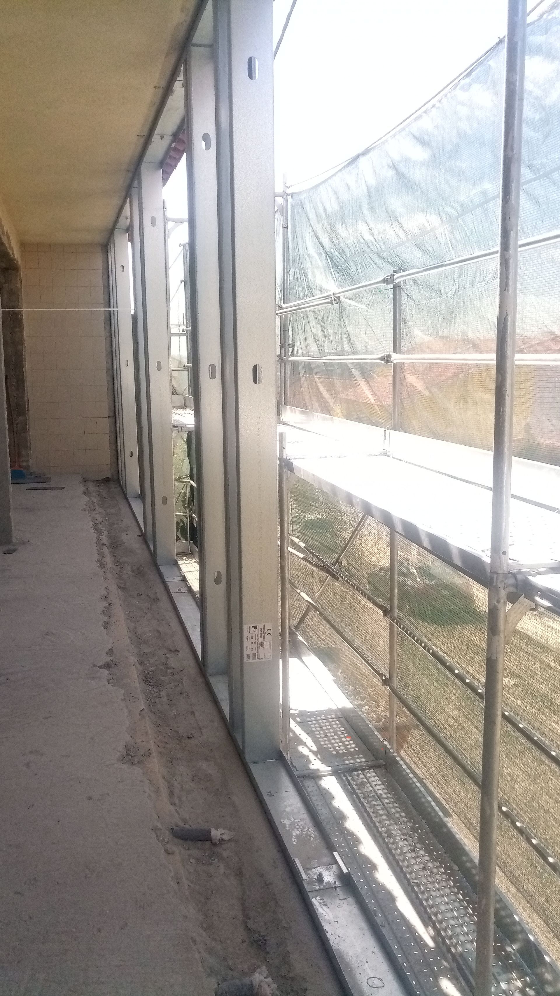 Caixilhos de aço de janelas em um prédio em construção, com andaimes visíveis do lado de fora.