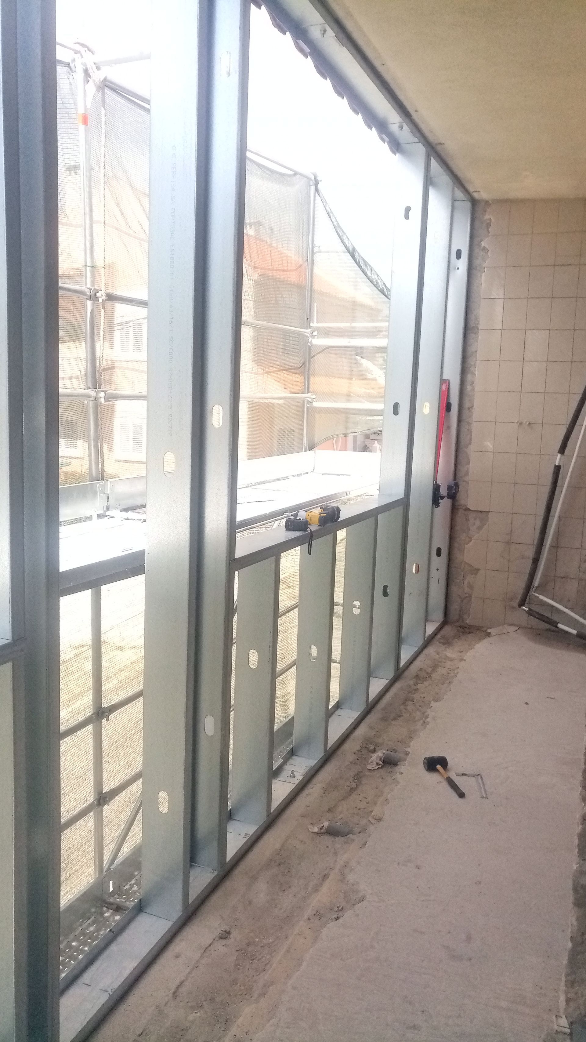 Estrutura metálica de uma janela, em um canteiro de obras no interior; vista para o exterior.