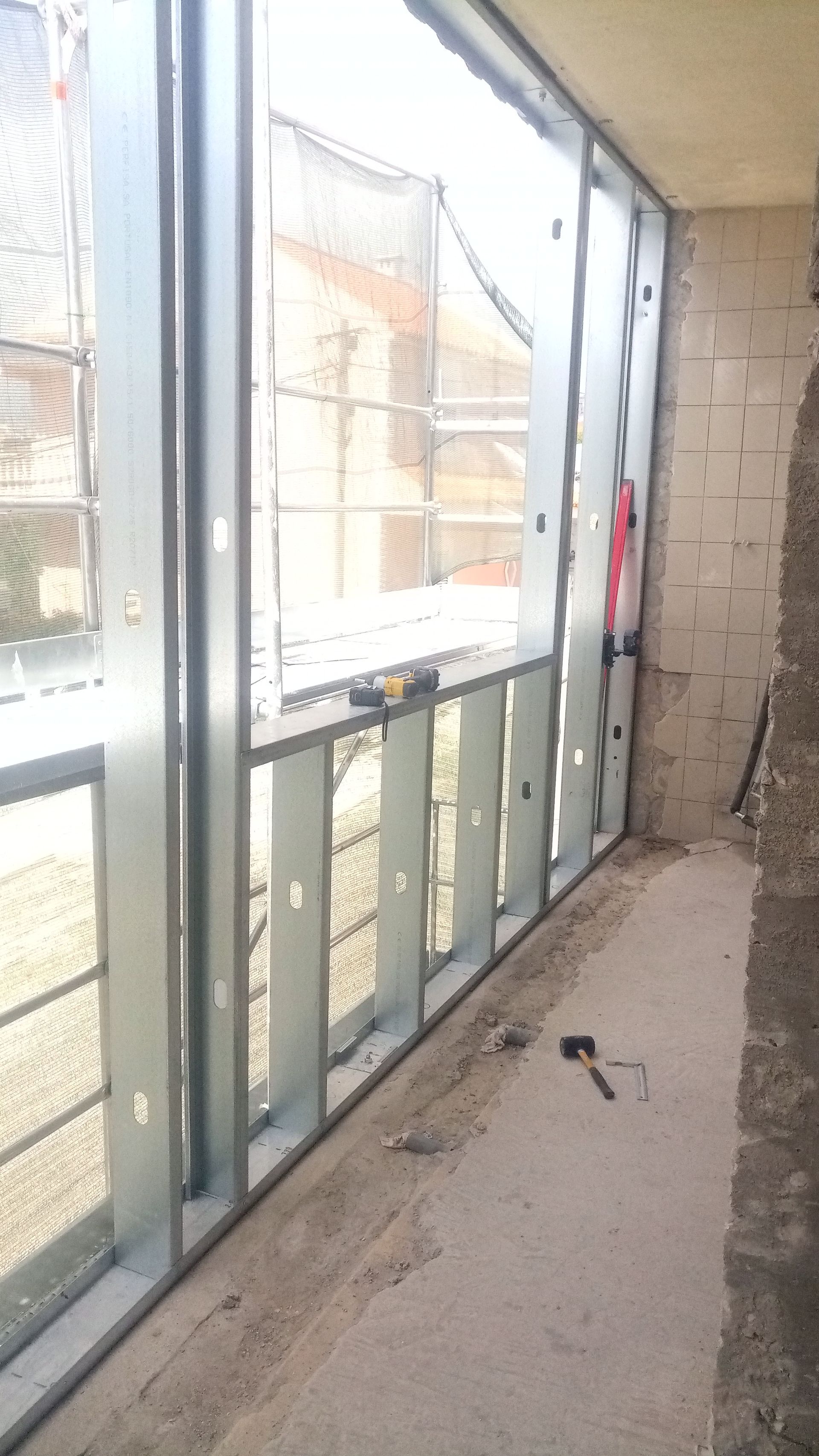 Estrutura metálica emoldurando uma janela e uma parede; construção interna em andamento.