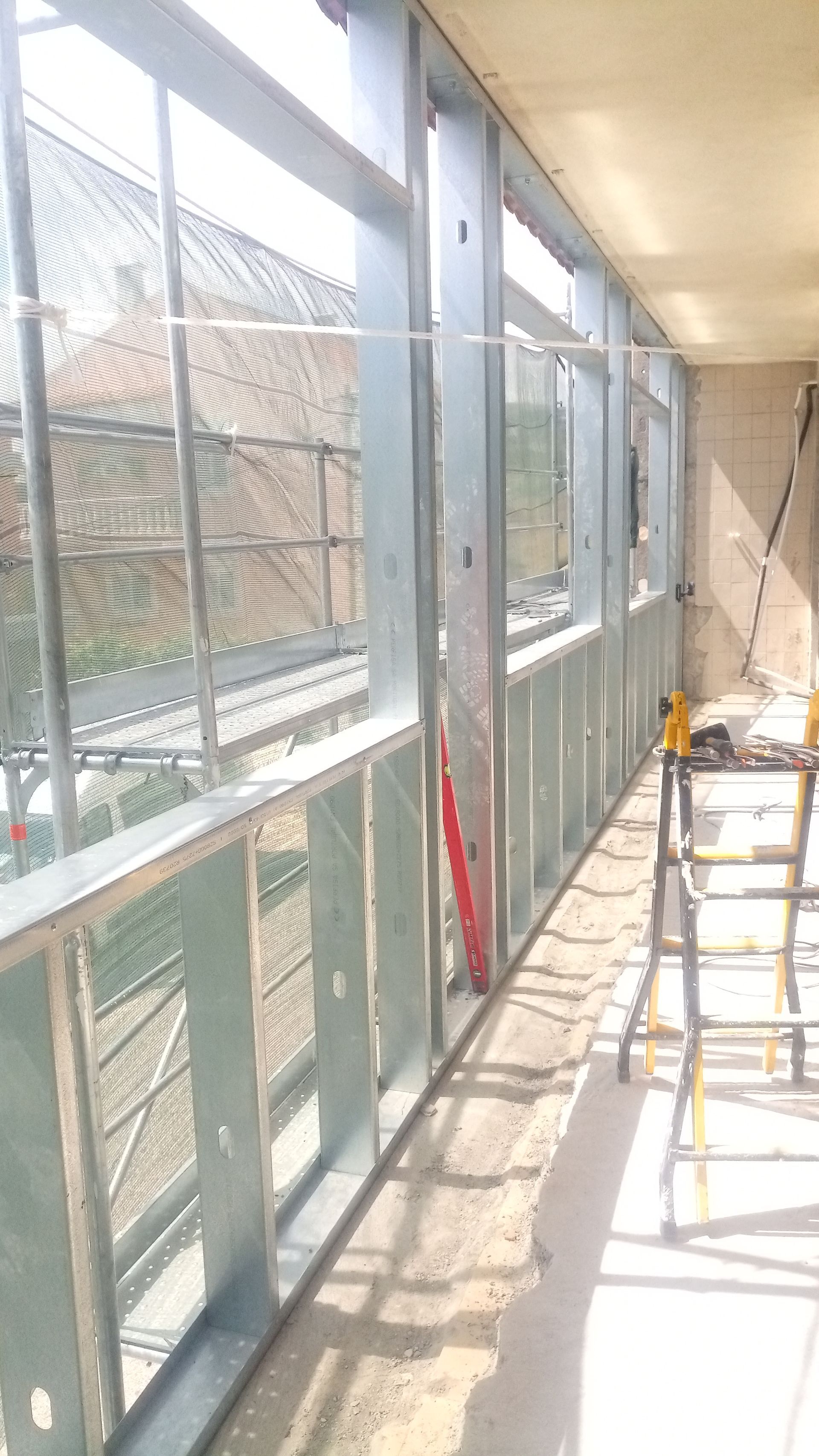 Estrutura metálica que delimita uma parede de janelas em construção. Andaimes visíveis do lado de fora.