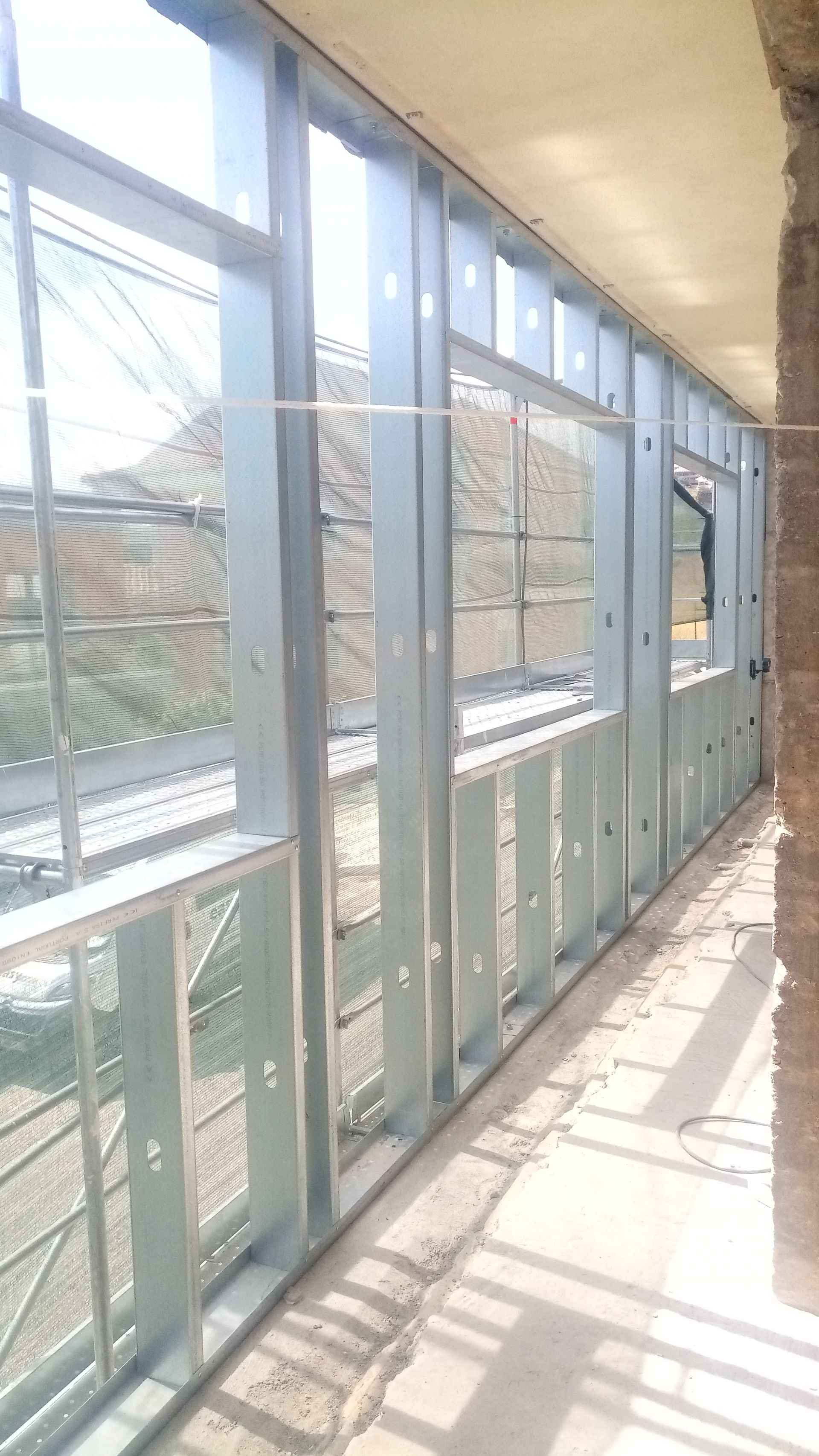 Estrutura metálica de uma parede com aberturas para janelas, no interior de um edifício inacabado.