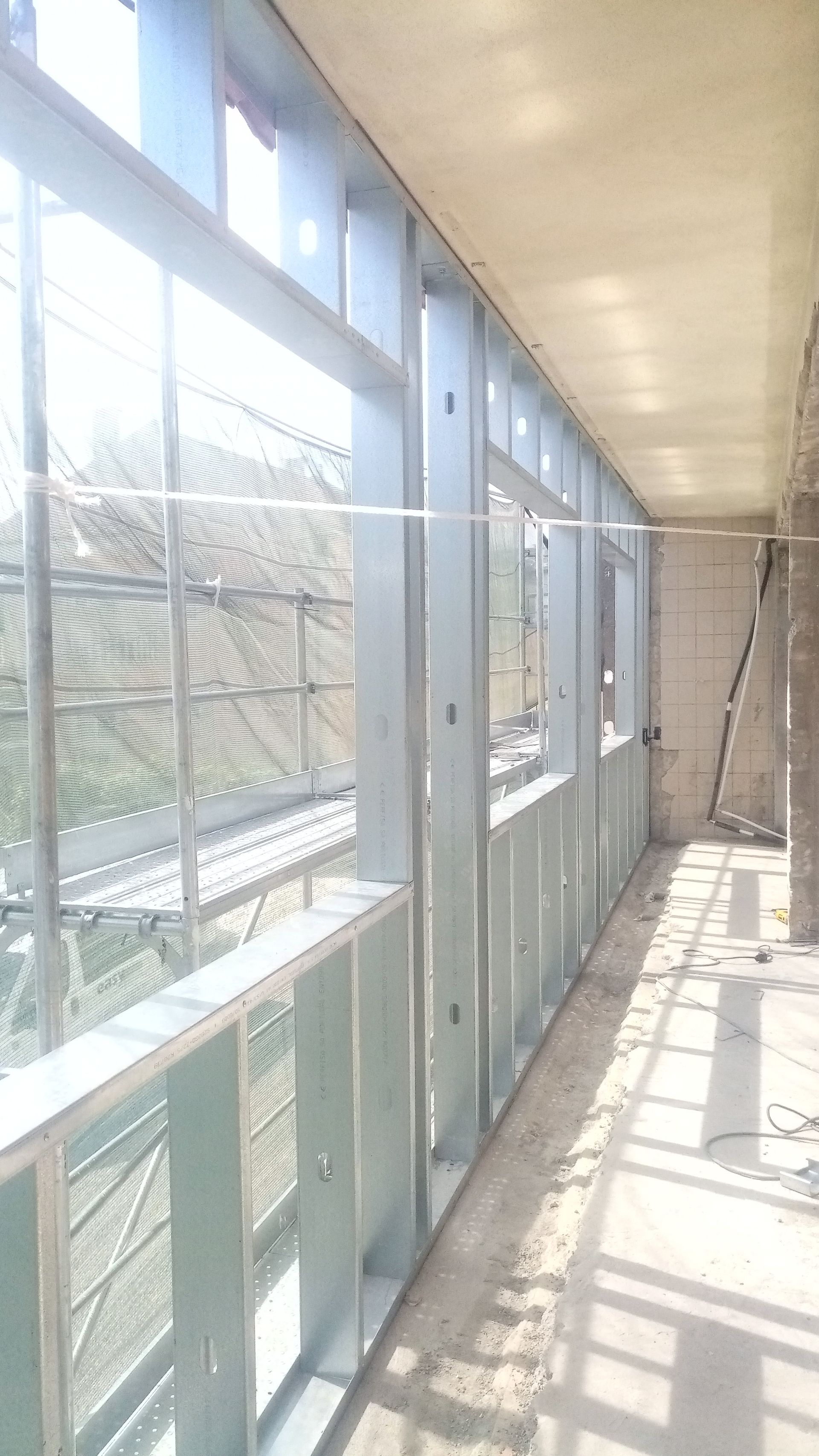 Estrutura metálica de uma parede, possivelmente interna, com luz natural visível através das aberturas das janelas.