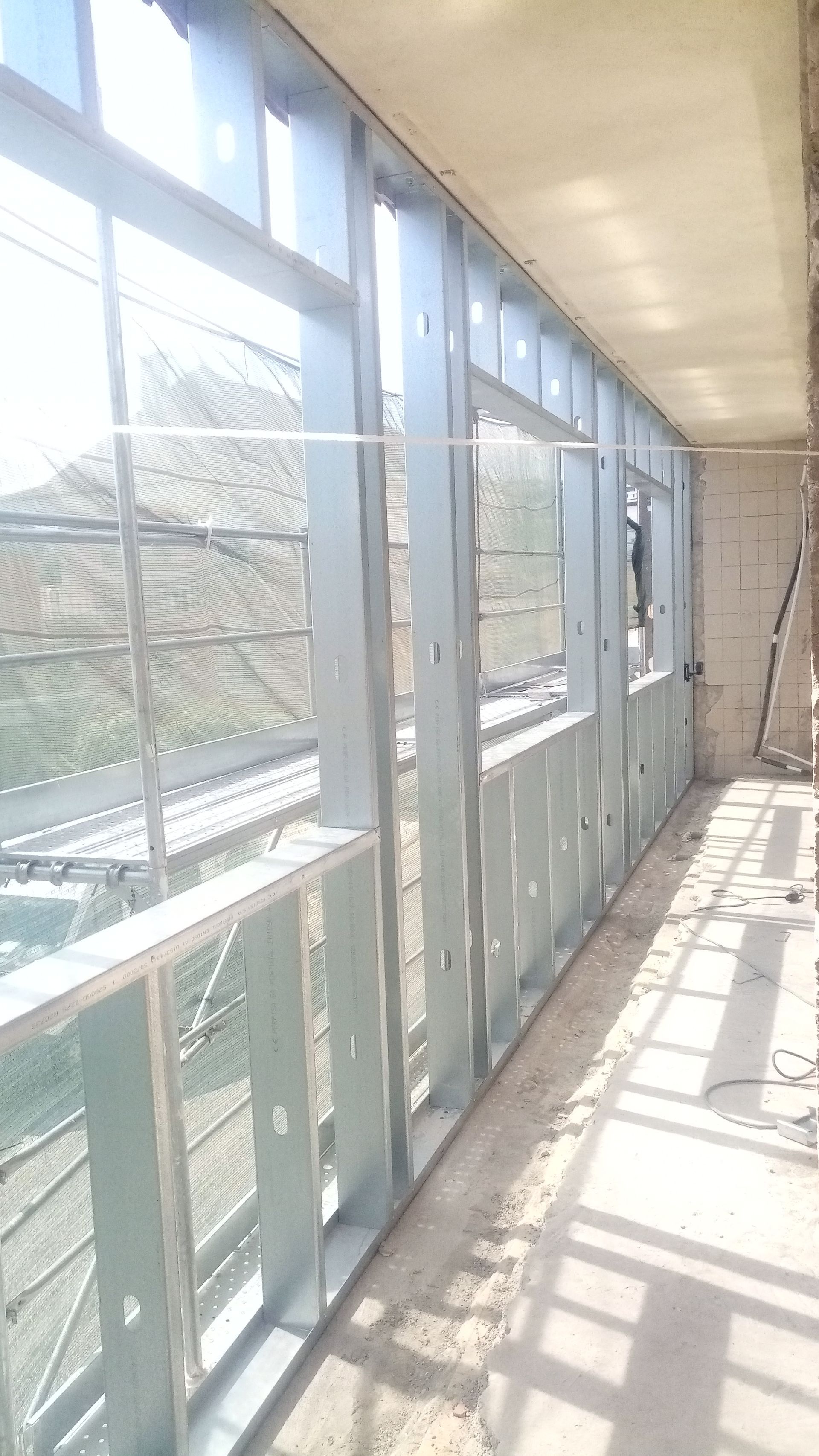 Interior de um canteiro de obras com estrutura metálica e vista para as colinas através das janelas.