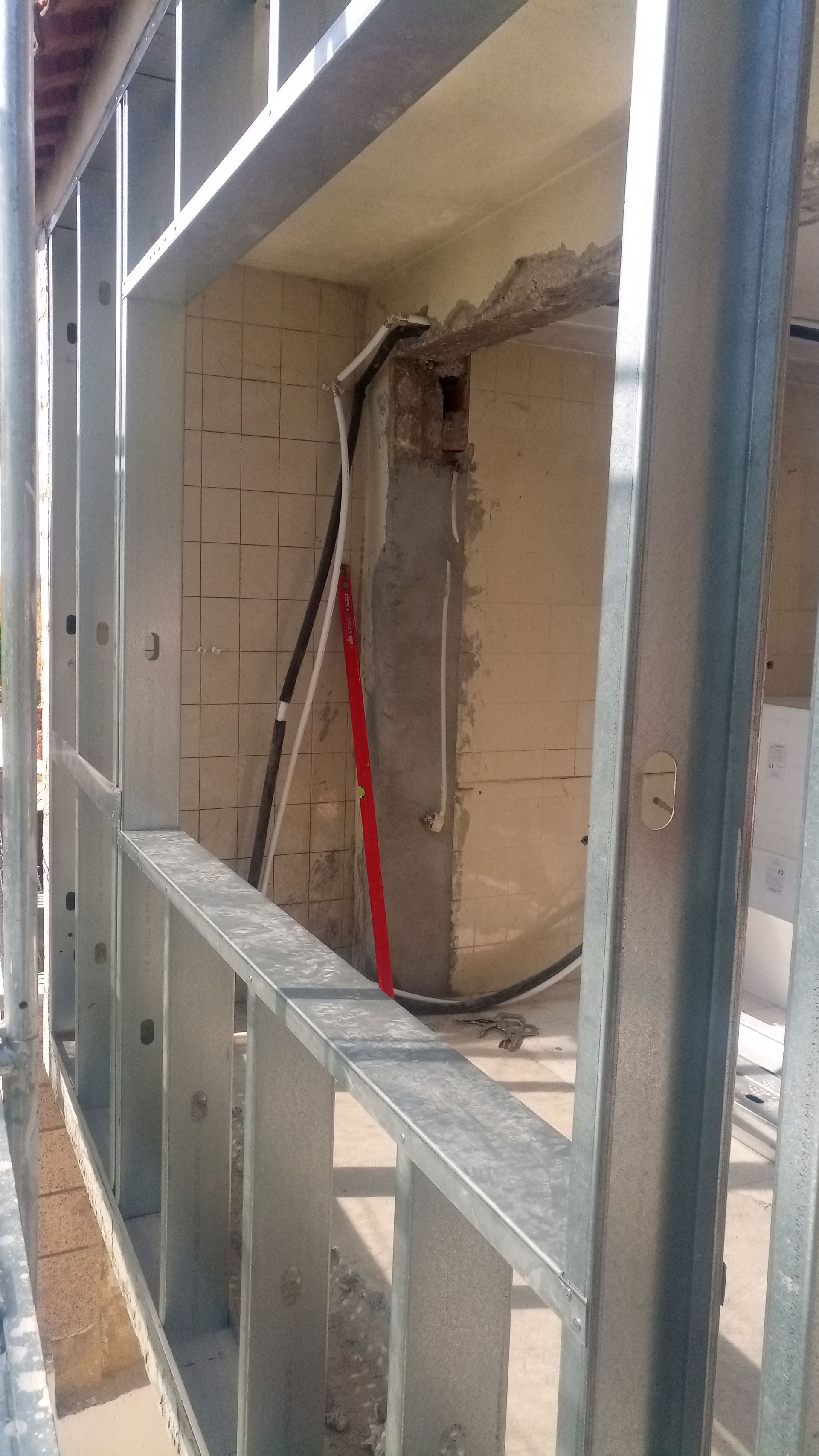 Estrutura metálica para construção de paredes, com tubulações e fios expostos visíveis em uma abertura.