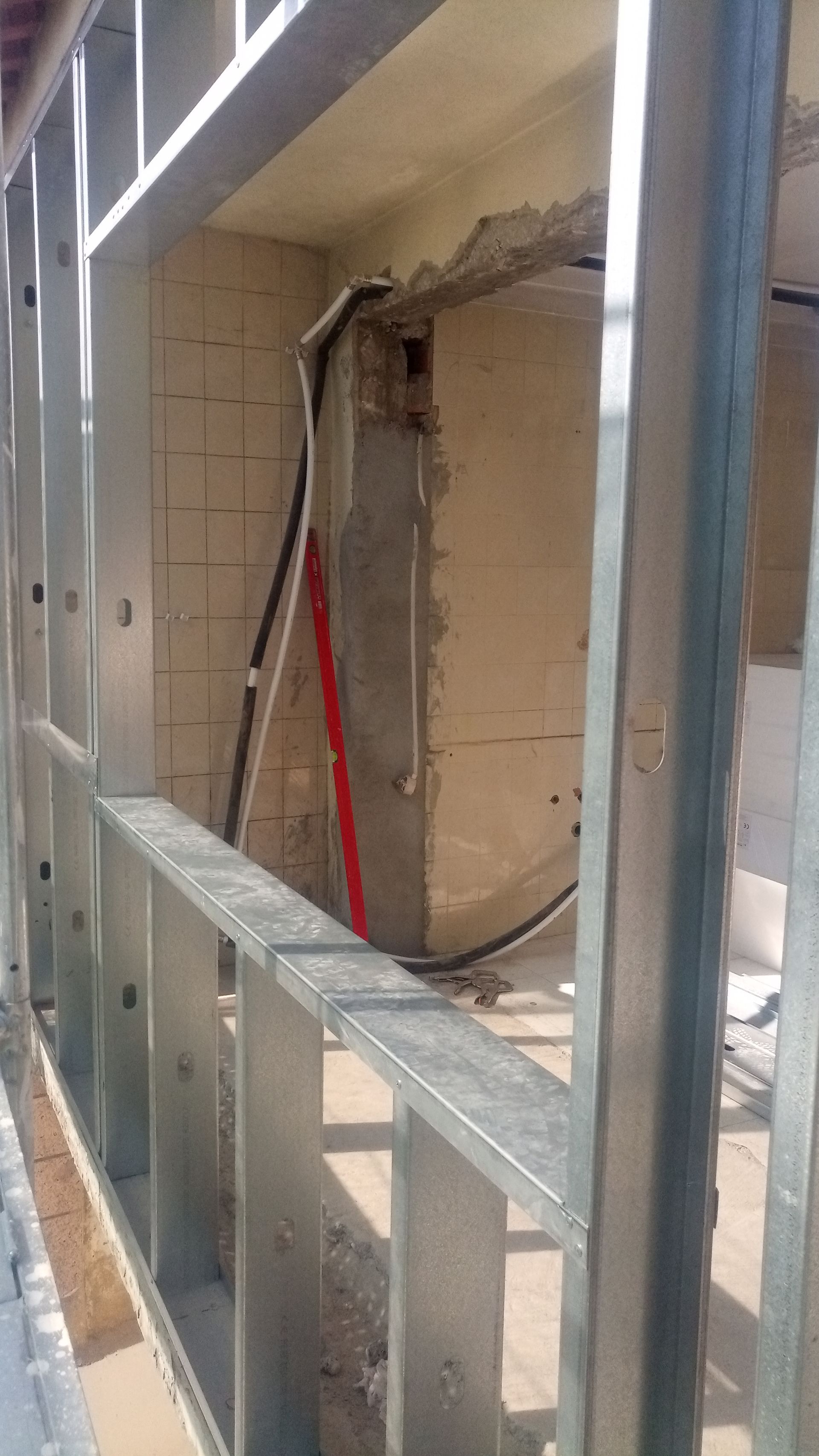 Estrutura metálica de uma parede com fiação elétrica visível e uma parede parcial de concreto em um canteiro de obras.