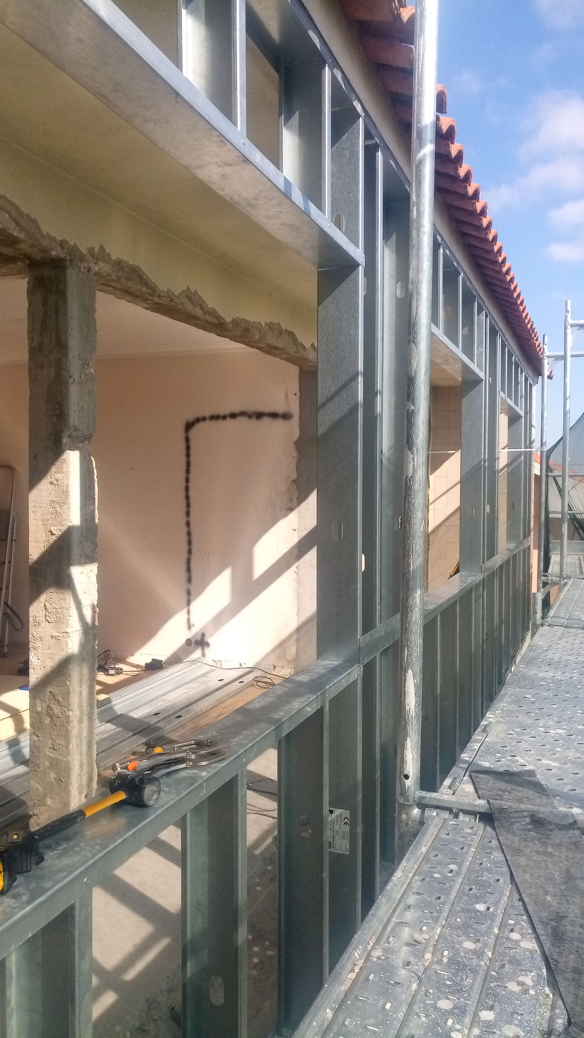 Estrutura metálica da parede externa de um edifício em construção, mostrando as aberturas das janelas e os andaimes.