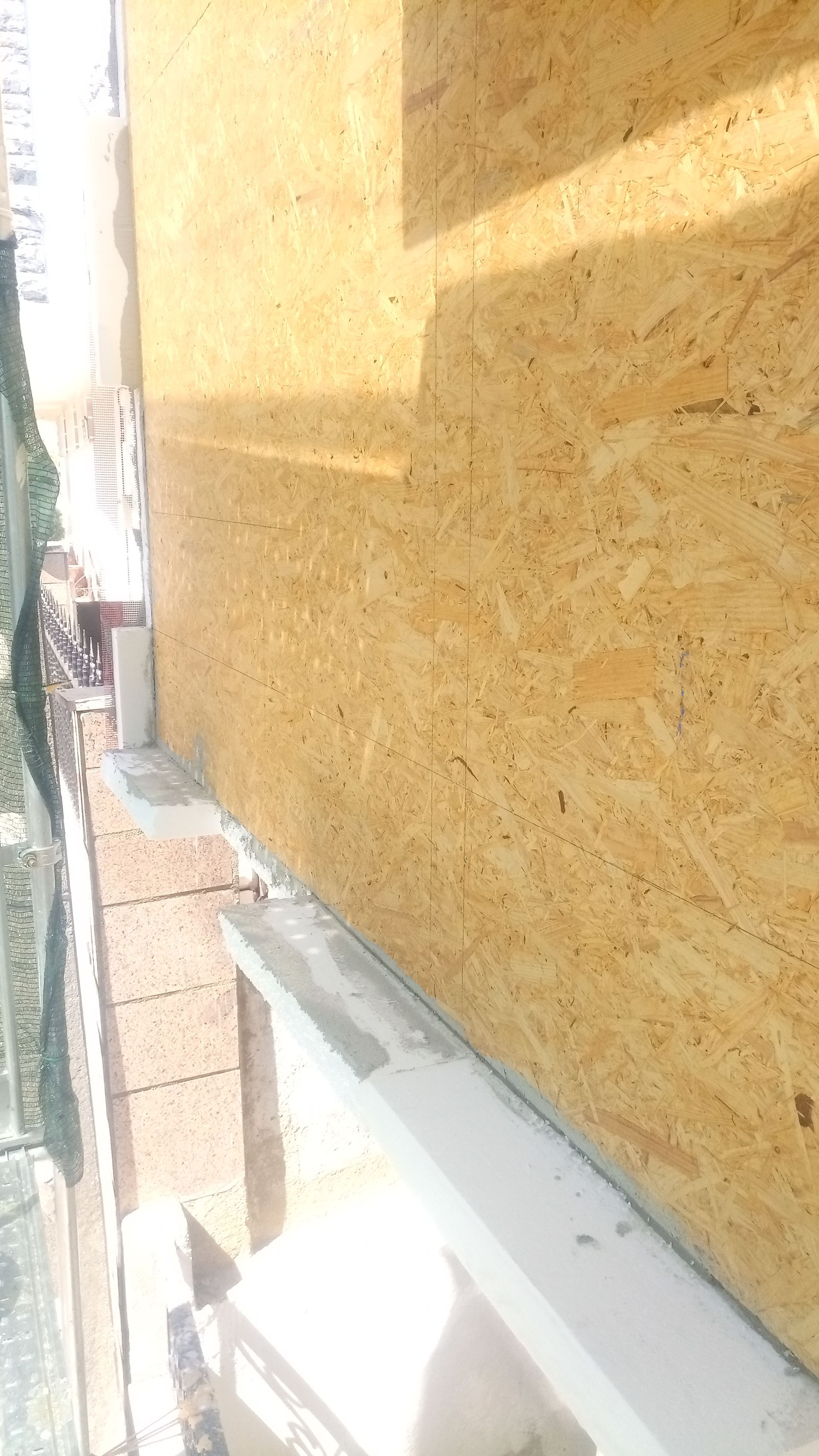 Vista exterior: Parede em OSB castanho-claro, beiral em tijolo e acabamento branco.