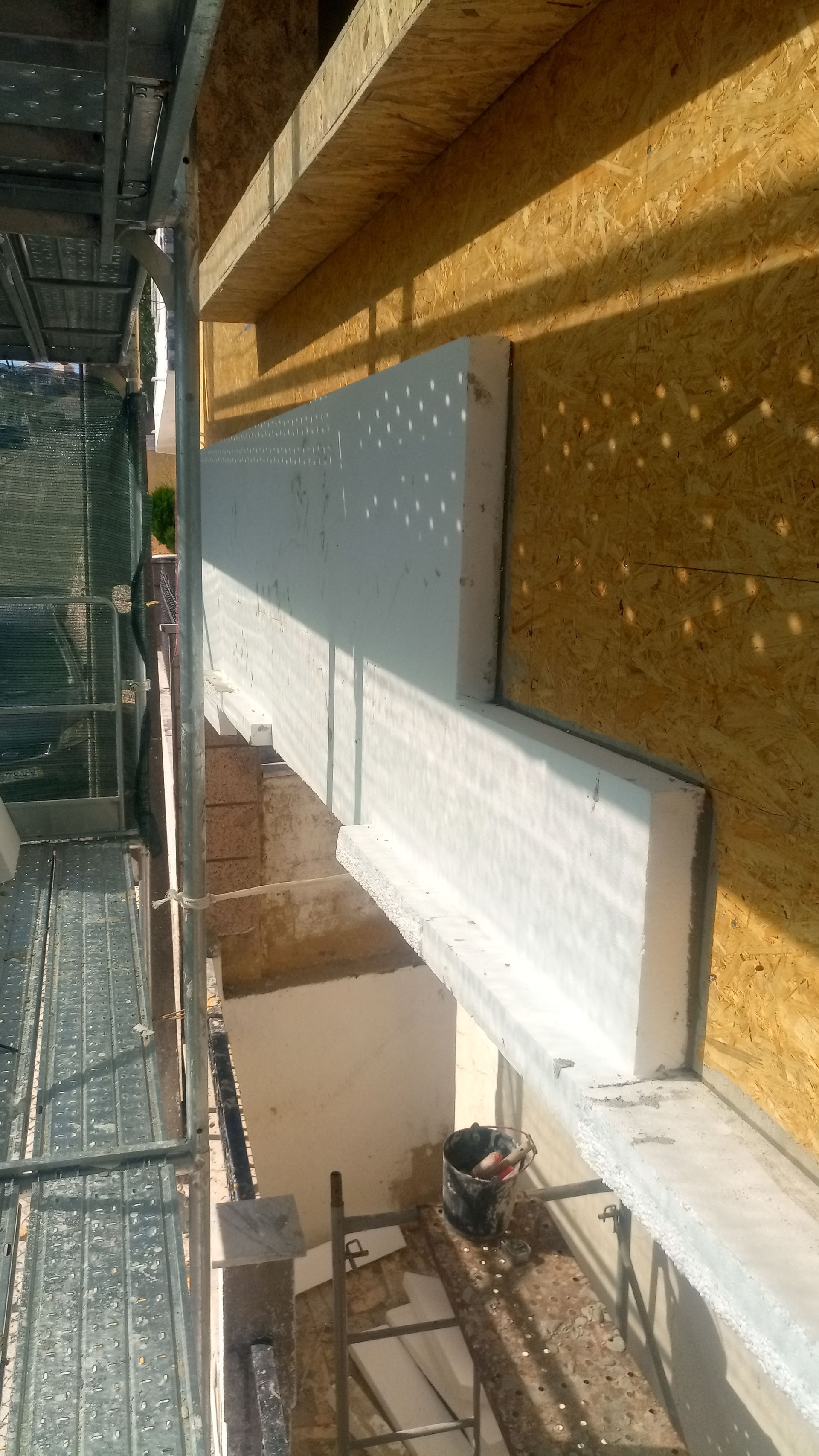 Canteiro de obras: Instalação de isolamento branco ao redor da moldura de uma janela. Andaimes visíveis.