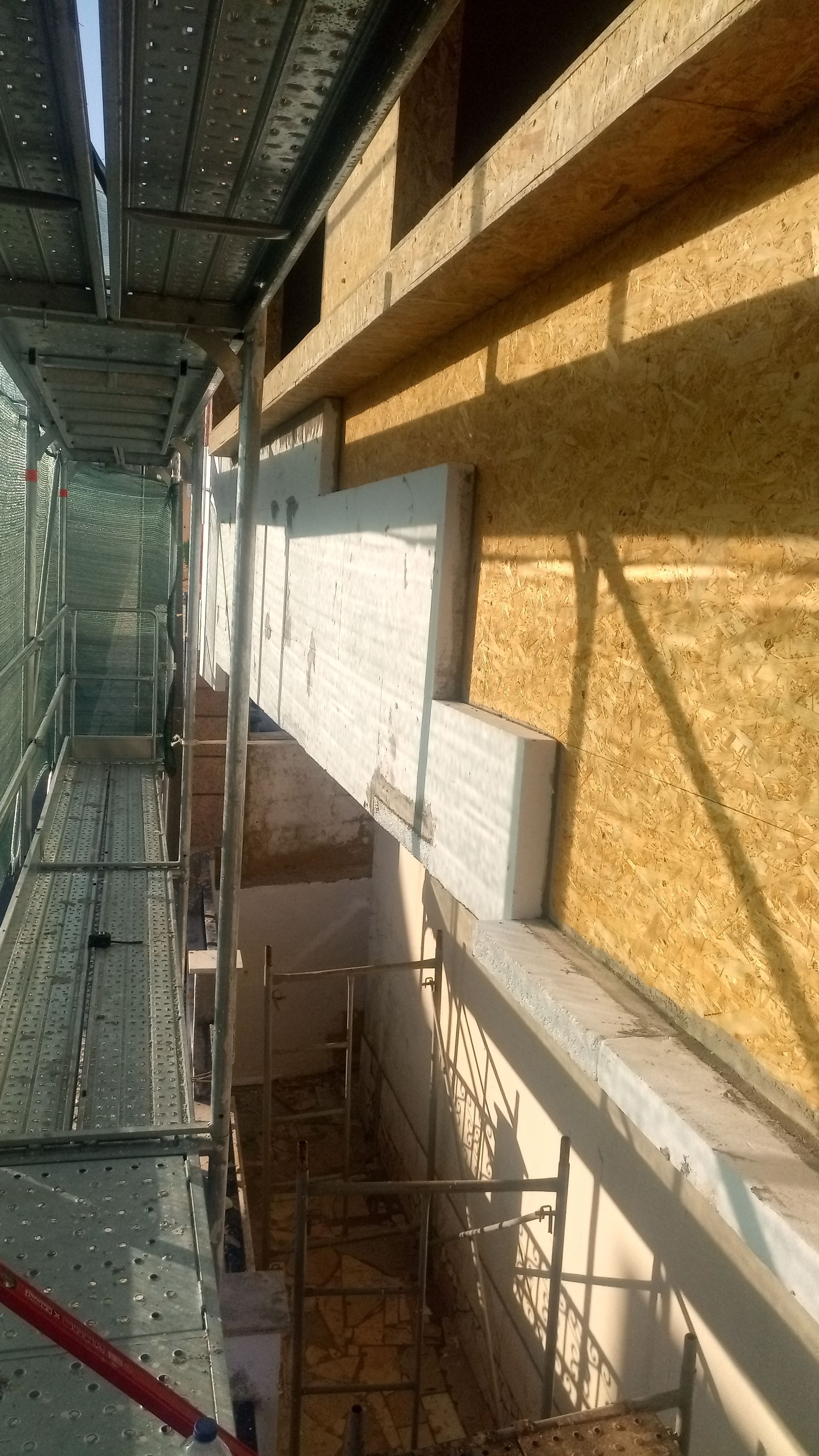 Andaimes de construção ao lado da fachada de um edifício. Estão sendo instalados isolamento e compensado.