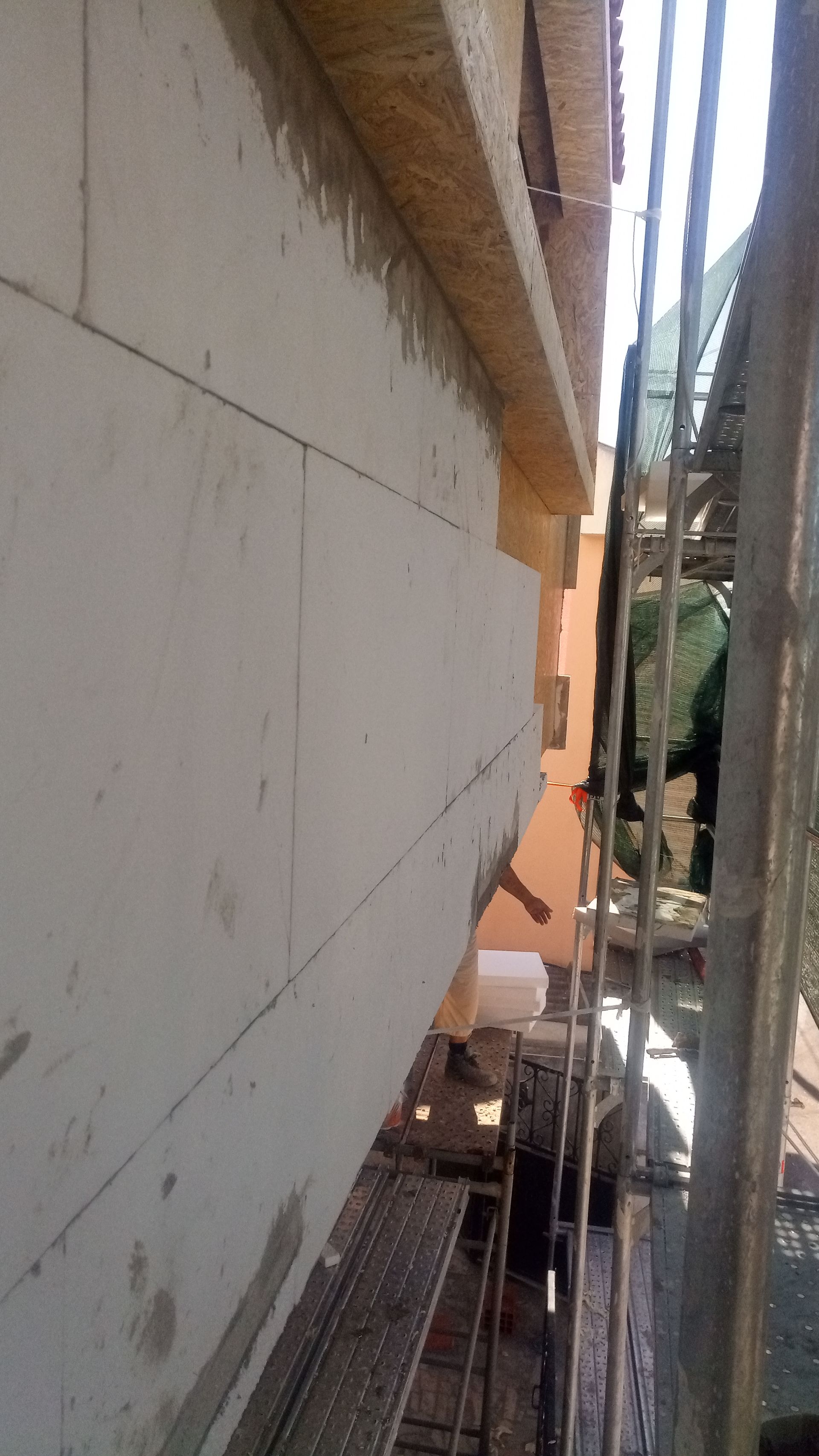 Parede externa em construção com painéis isolantes brancos e andaimes.