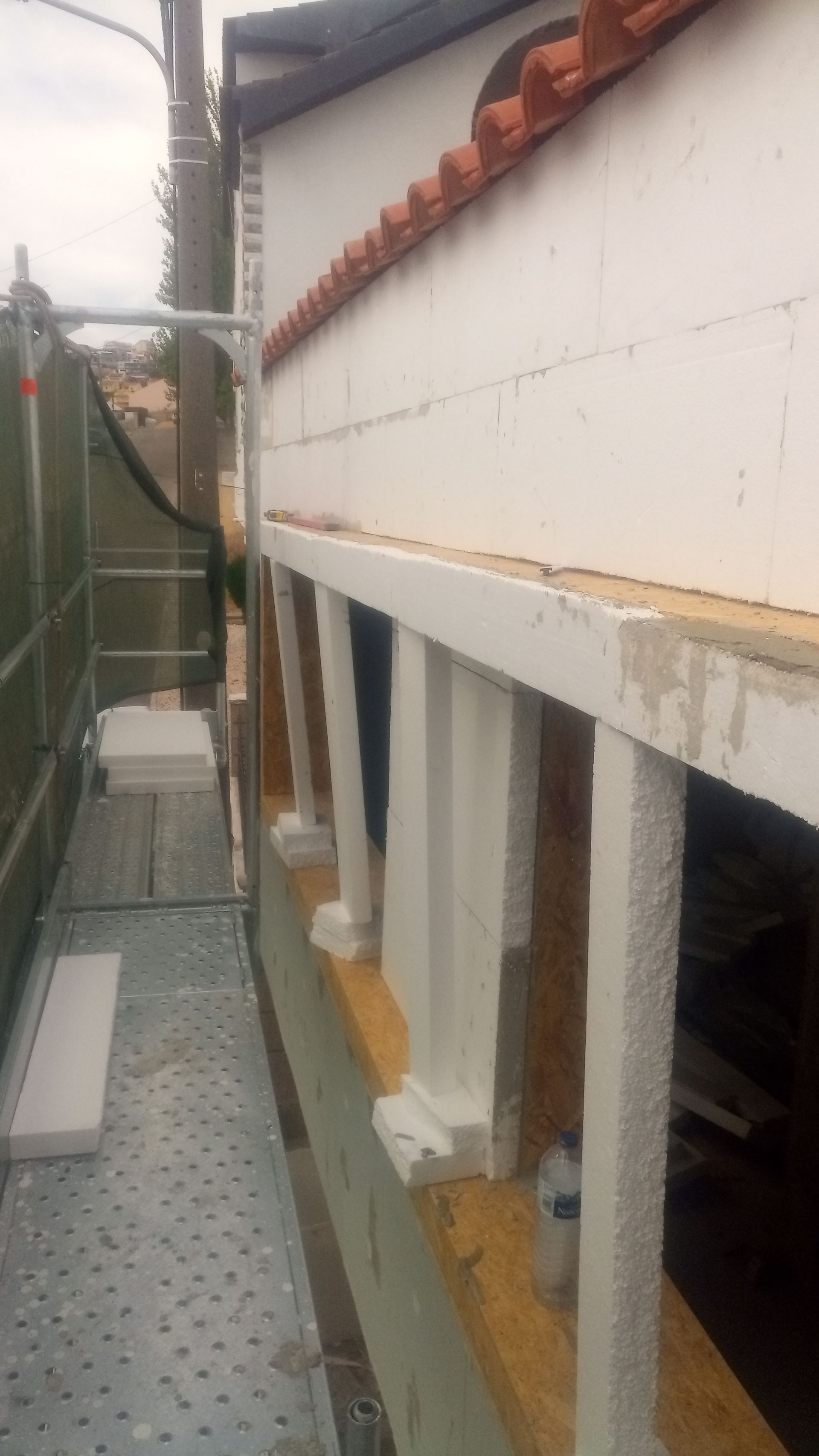 Reforma da fachada do prédio em andamento; andaimes ao lado de uma parede com pilares pintados de branco.