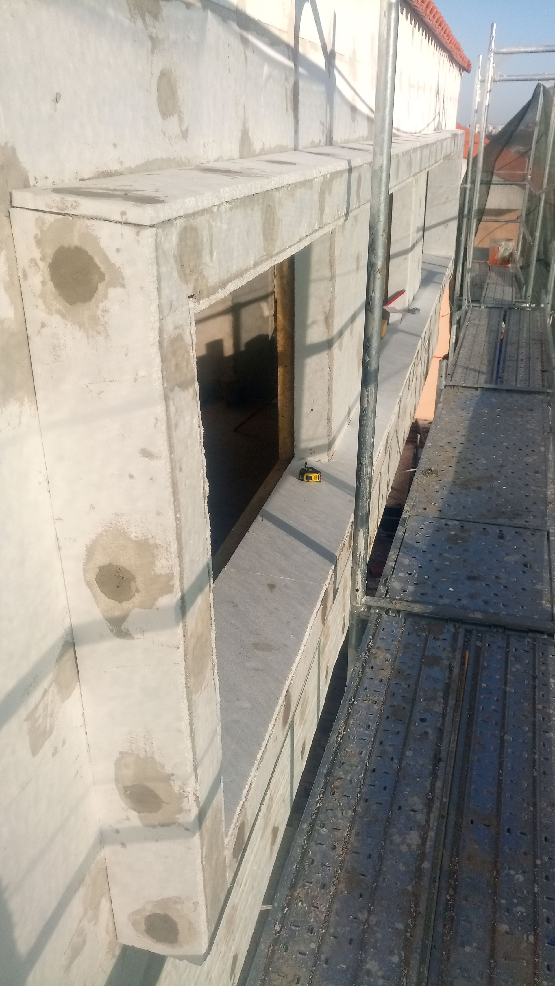 Construção de caixilho de janela com andaimes. Blocos cinza-claros em volta de uma janela marrom, em área externa.