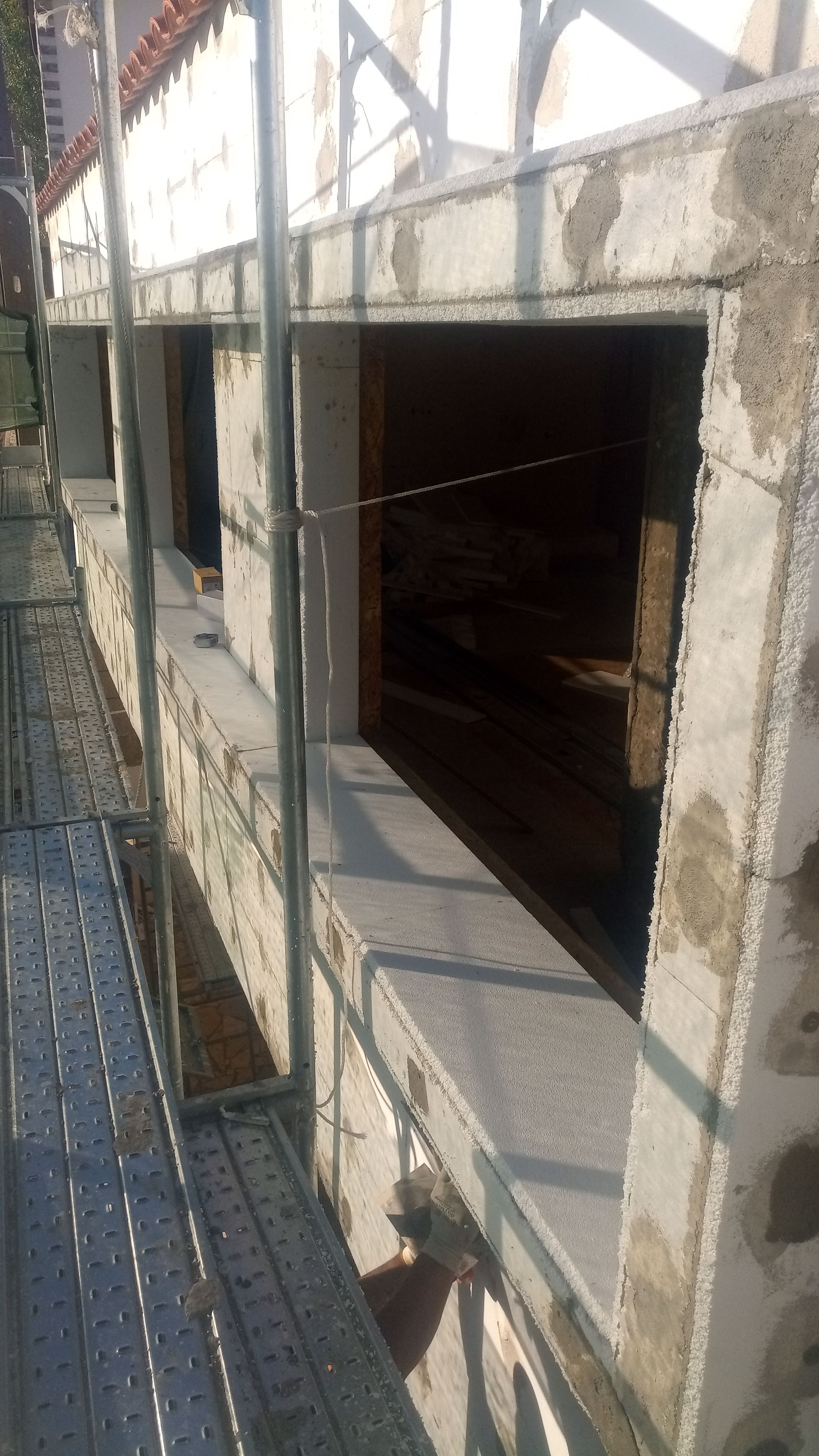 Canteiro de obras: caixilhos de janelas instalados em parede de concreto com andaimes visíveis; parcialmente concluído.