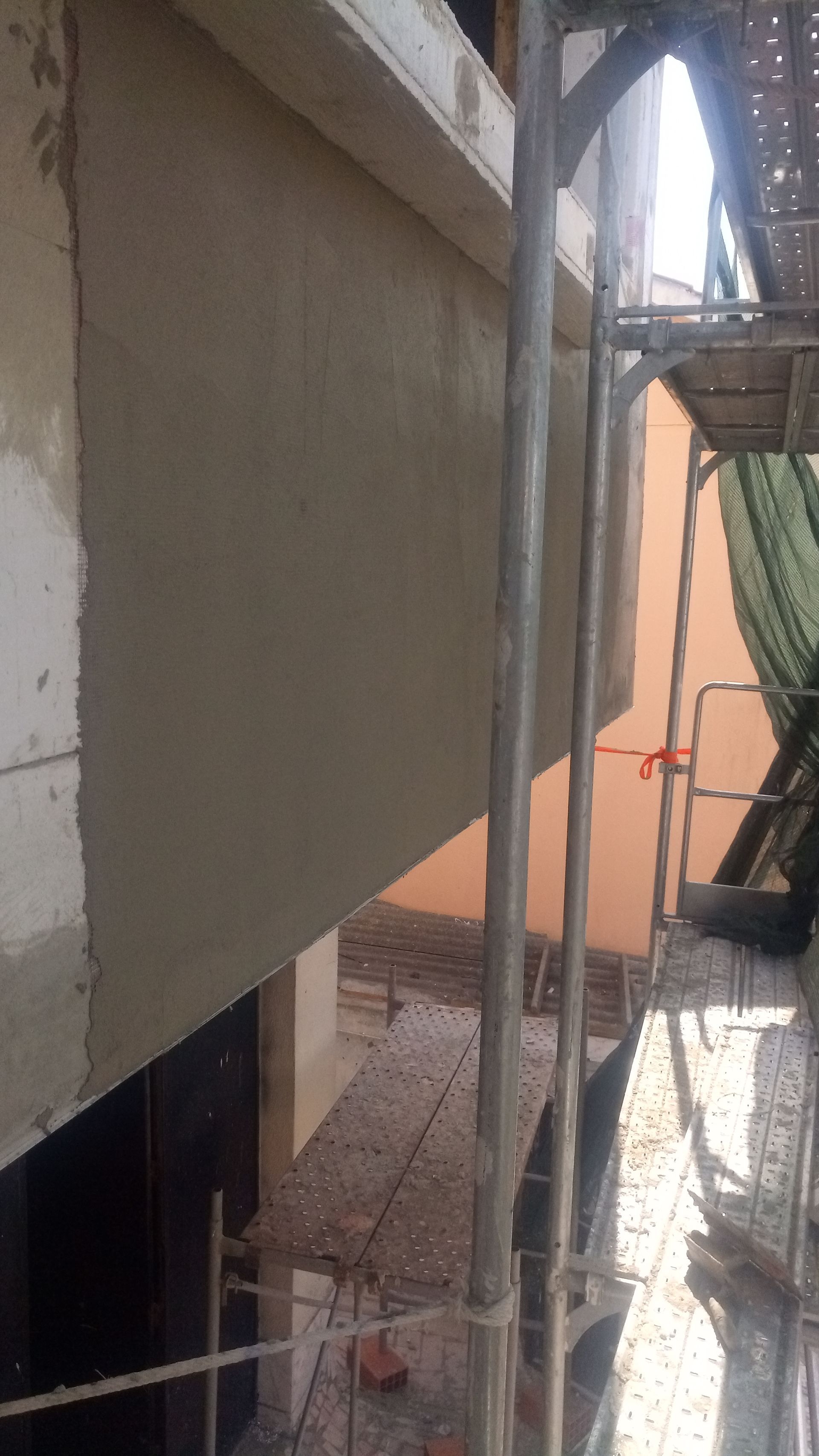 Exterior do edifício com parede recém-rebocada, andaimes visíveis.