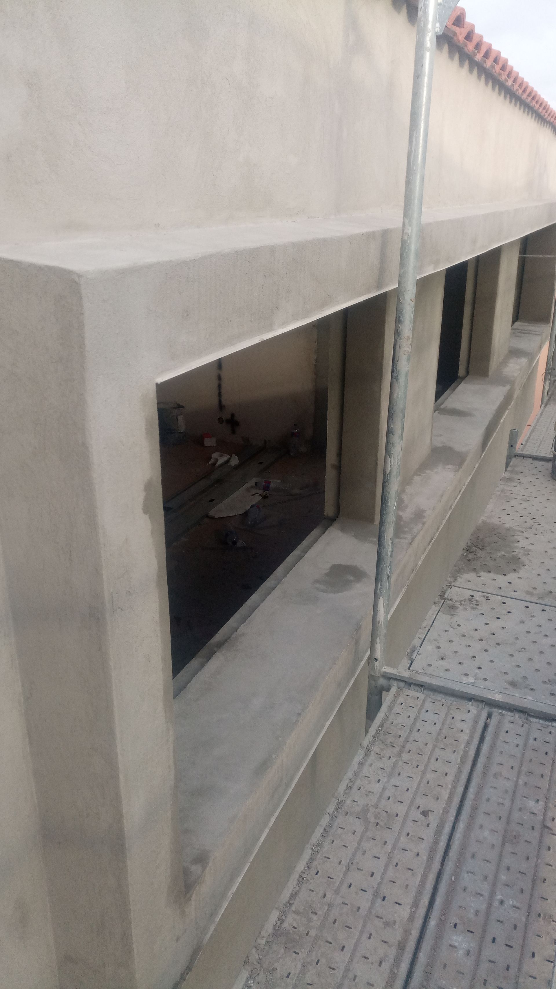 Parede externa com caixilhos de janelas inacabados, andaimes e materiais de construção visíveis no interior.