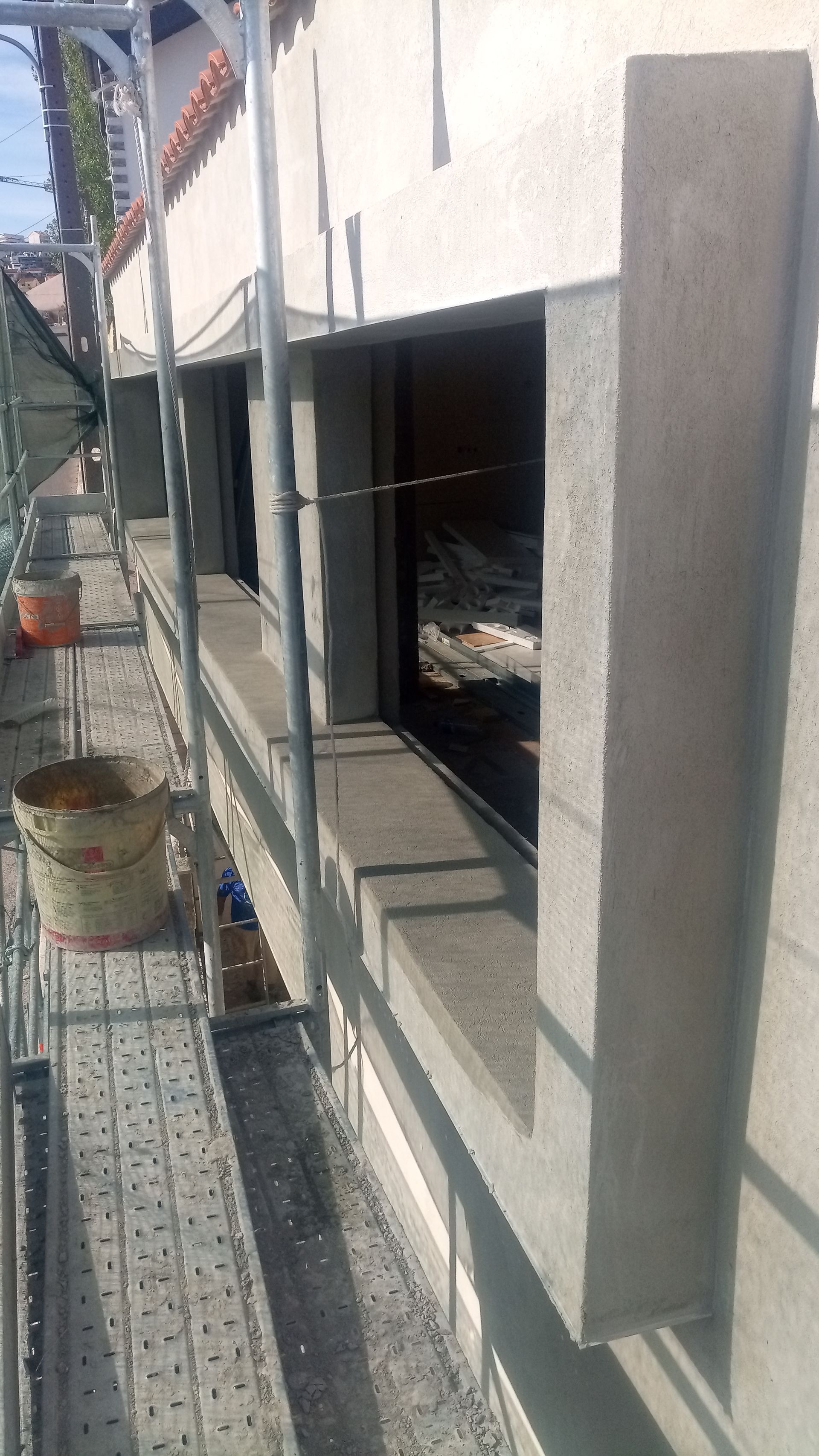 Exterior de um edifício em construção com andaimes em volta das janelas; estruturas de cimento visíveis.