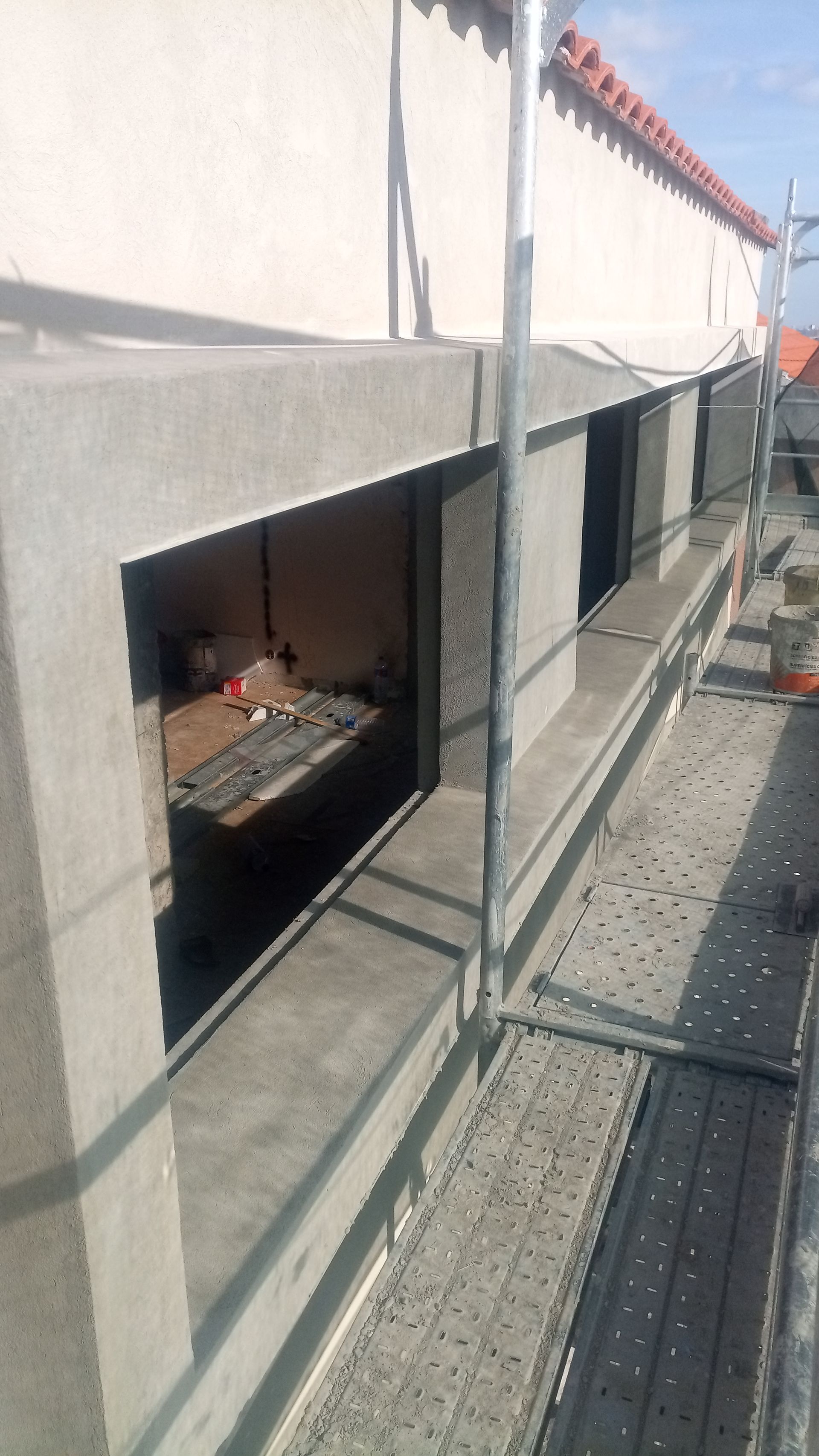 Canteiro de obras com caixilhos de concreto para janelas, andaimes e telhado.