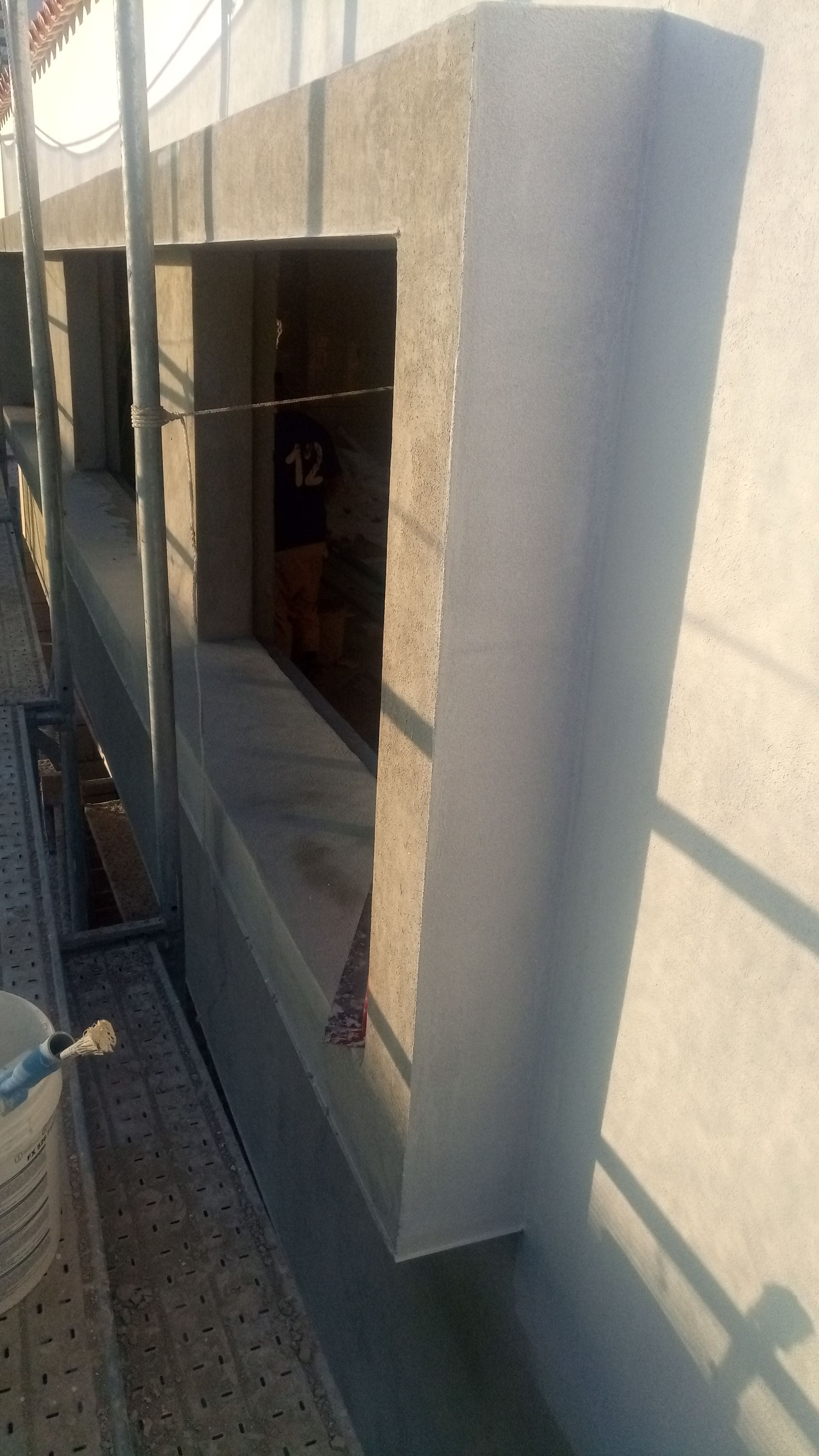 Vista externa da estrutura de concreto da janela, recém-rebocada. Andaime e plataforma elevatória visíveis.