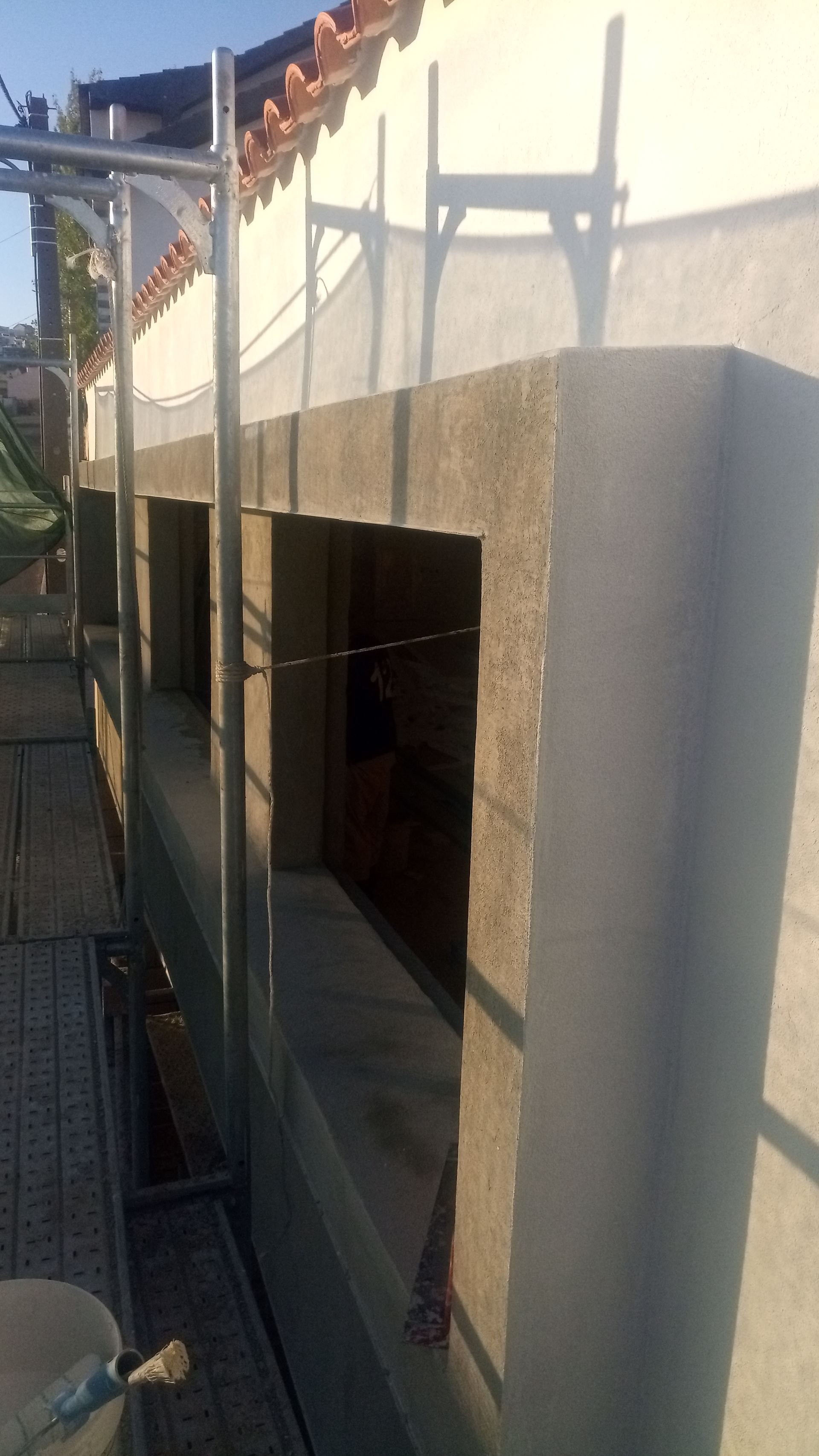 Parede externa com caixilhos de janelas inacabados, andaimes e telhas laranja.