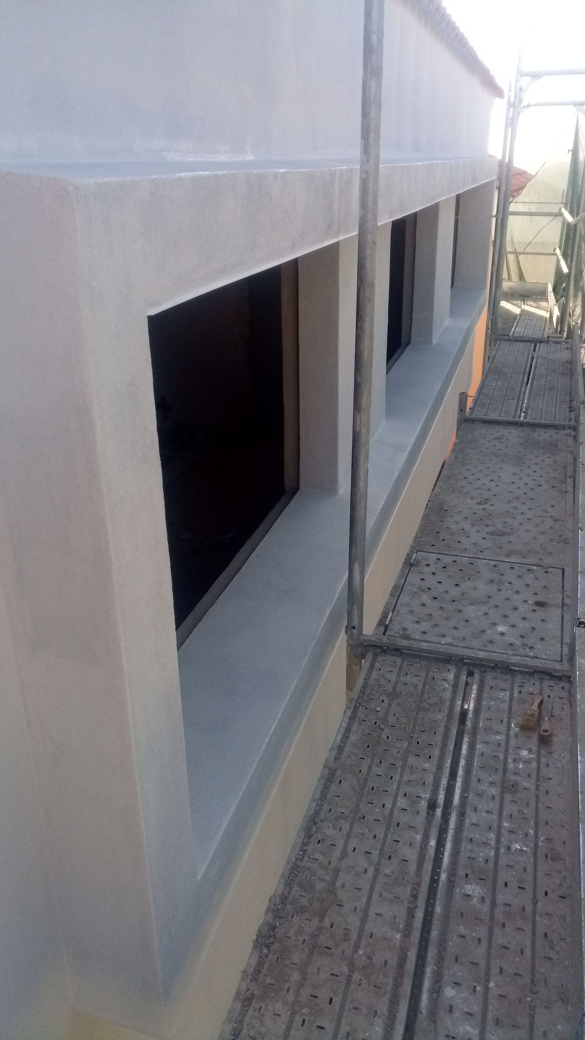 Fachada do edifício com várias janelas retangulares e andaimes na lateral.