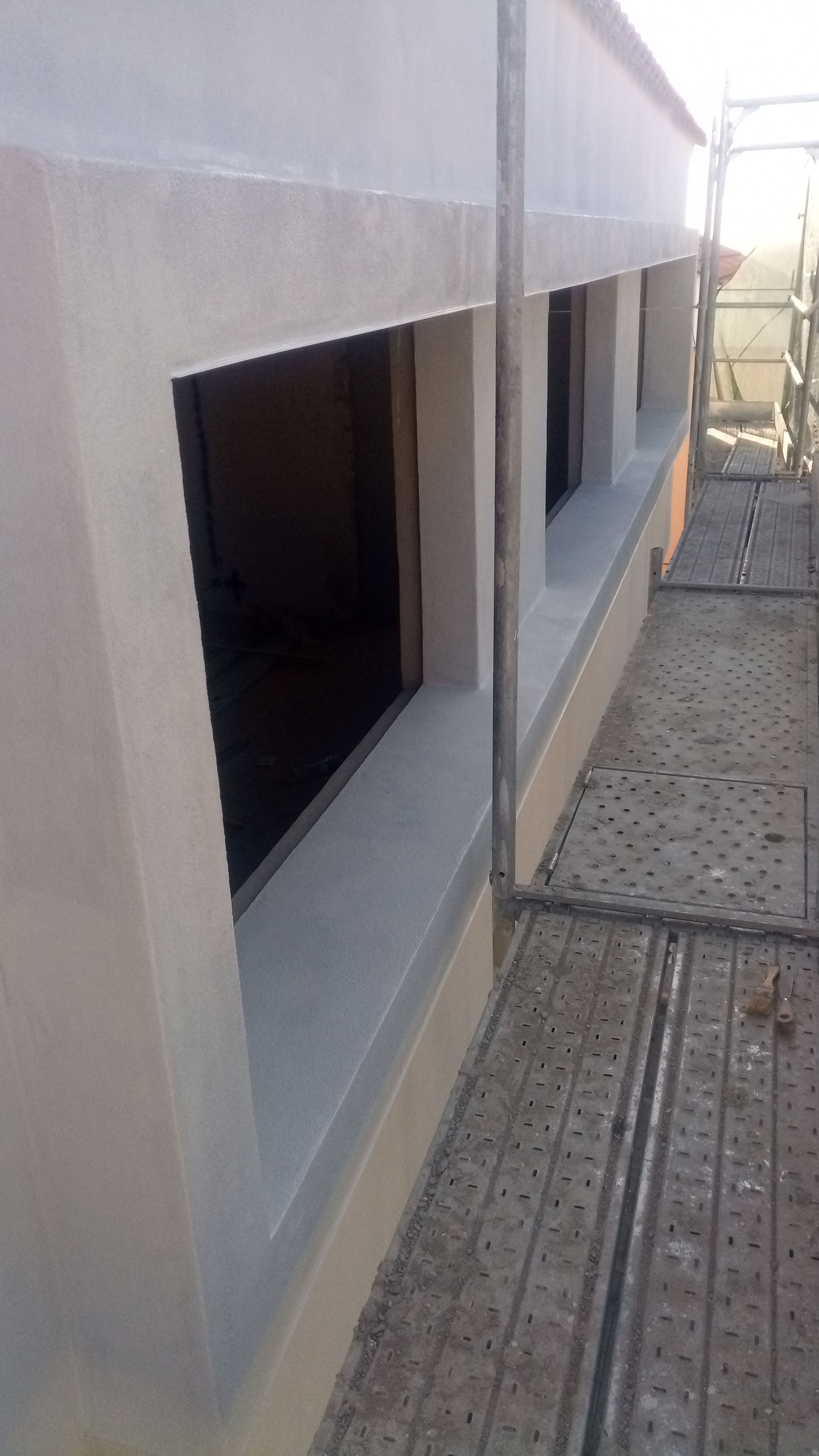 Exterior do edifício com três aberturas retangulares para janelas, andaimes e paredes em tom bege claro.