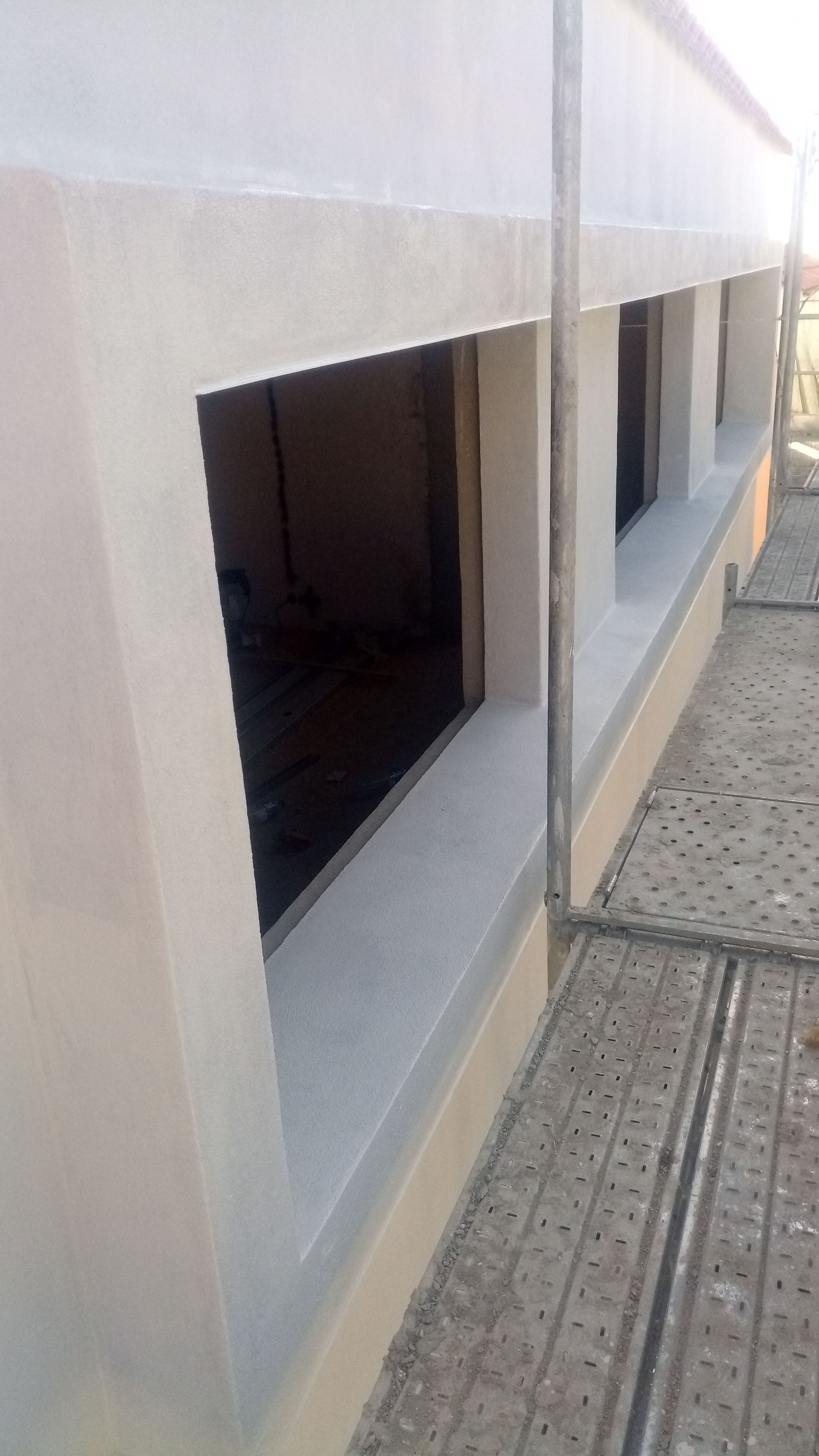 Fachada do edifício com várias janelas retangulares, pintada de bege claro. Andaimes visíveis.