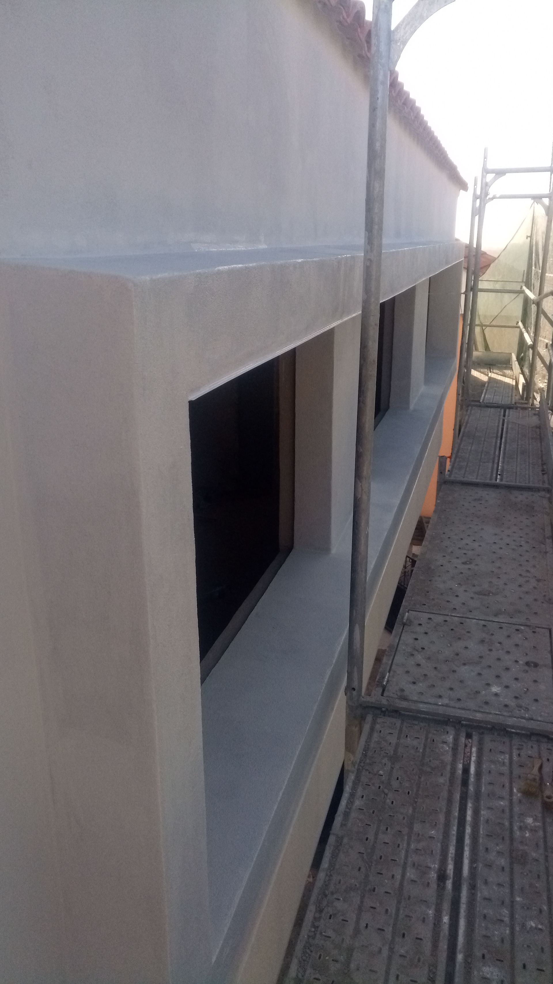 Exterior de um edifício com várias janelas; estuque e acabamentos em tons claros, vidros escuros, presença de andaimes.