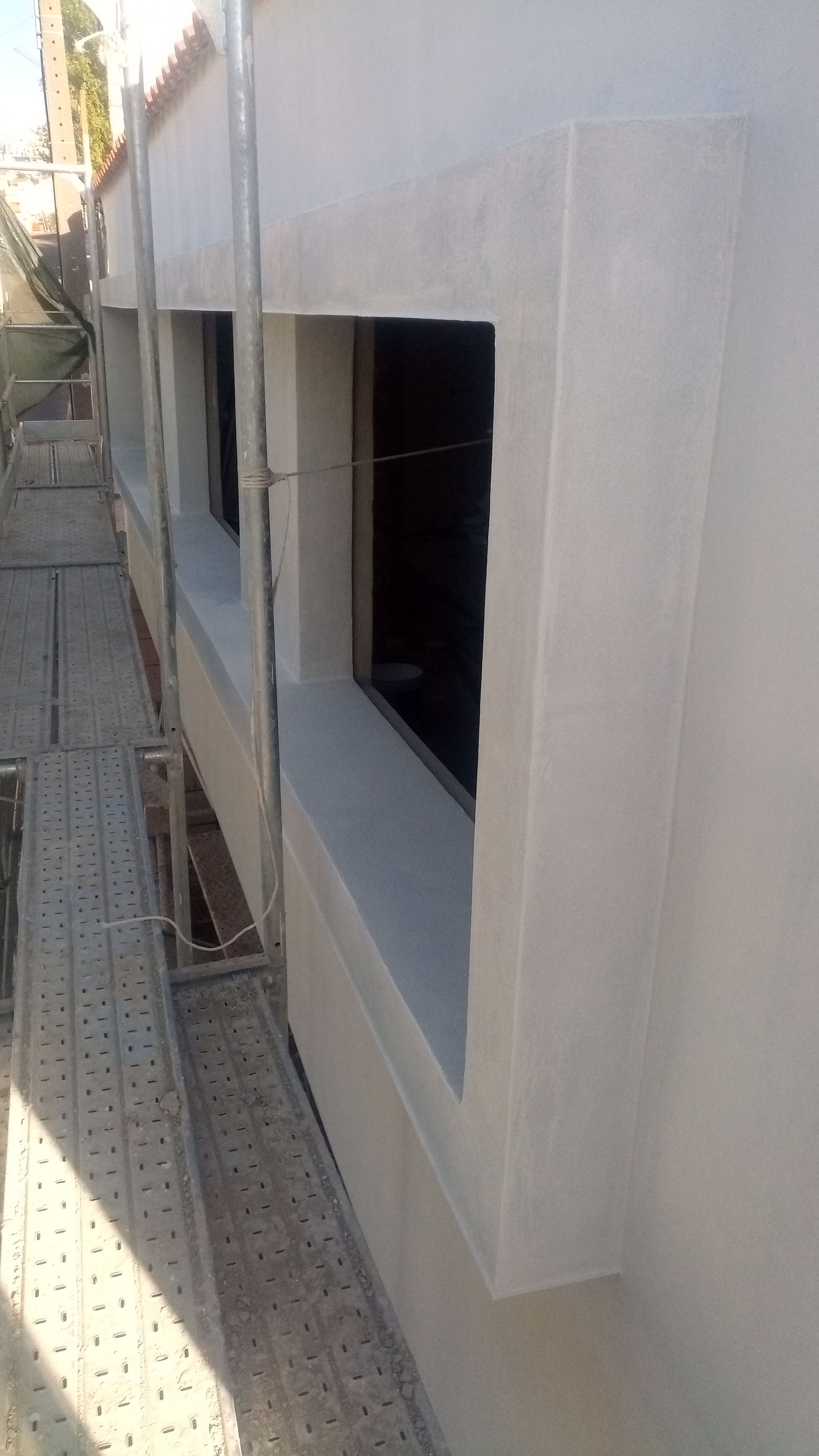 Parede externa com janelas retangulares, andaimes laterais e acabamento em cor clara.